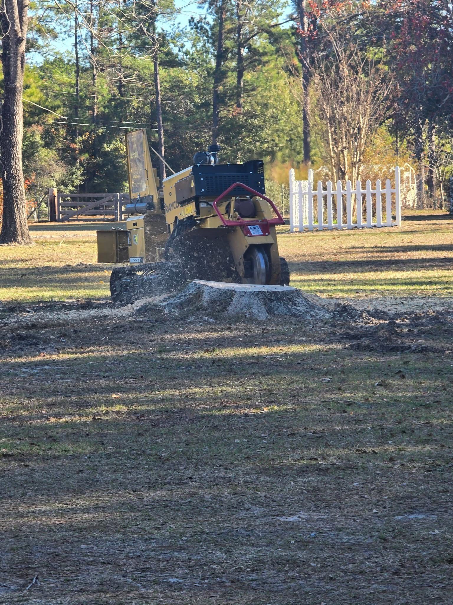 Small yellow tractor pushing gravel in a grassy yard with trees and a white fence in the background
