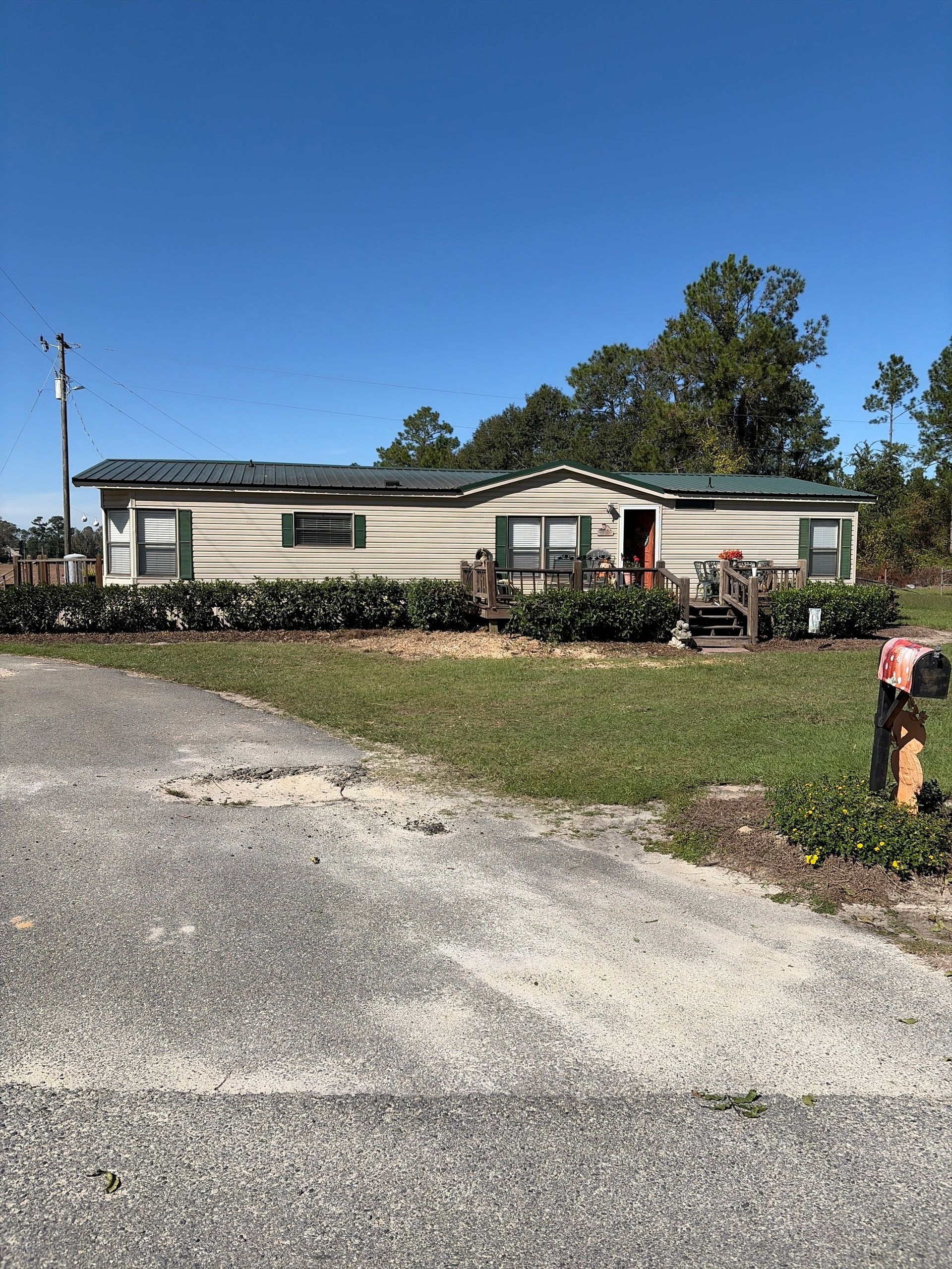 Single-story beige house with a gravel driveway, green lawn, and clear blue sky.