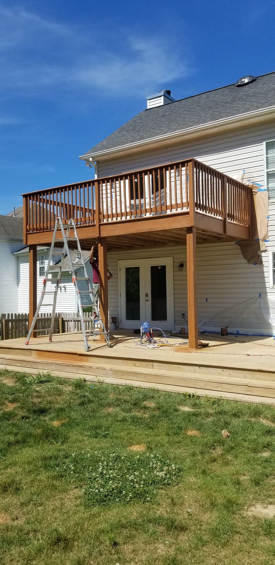 White house with a wooden balcony deck and ladder under construction on a sunny day
