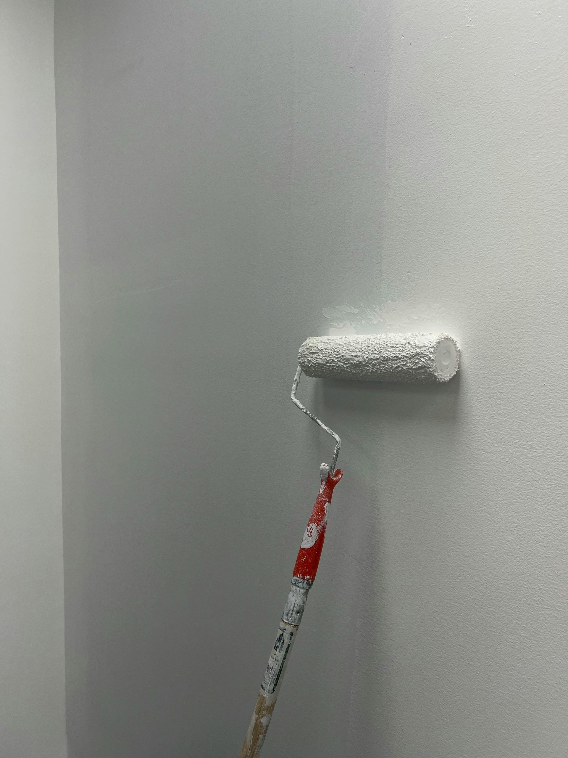 A white paint roller applying white paint to a light gray wall.