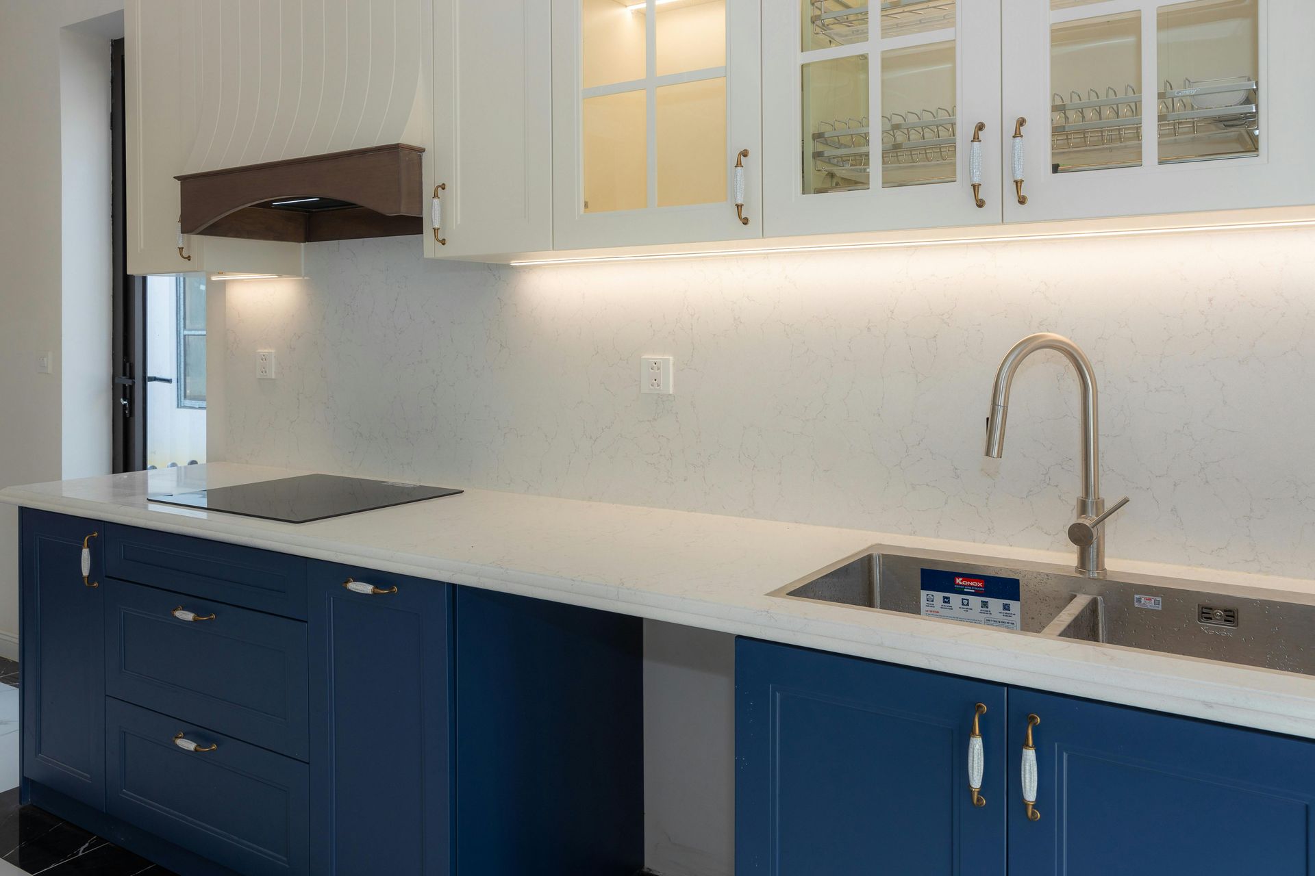 A modern kitchen with deep blue lower cabinets, white countertops, and white upper cabinets with glass-front doors.