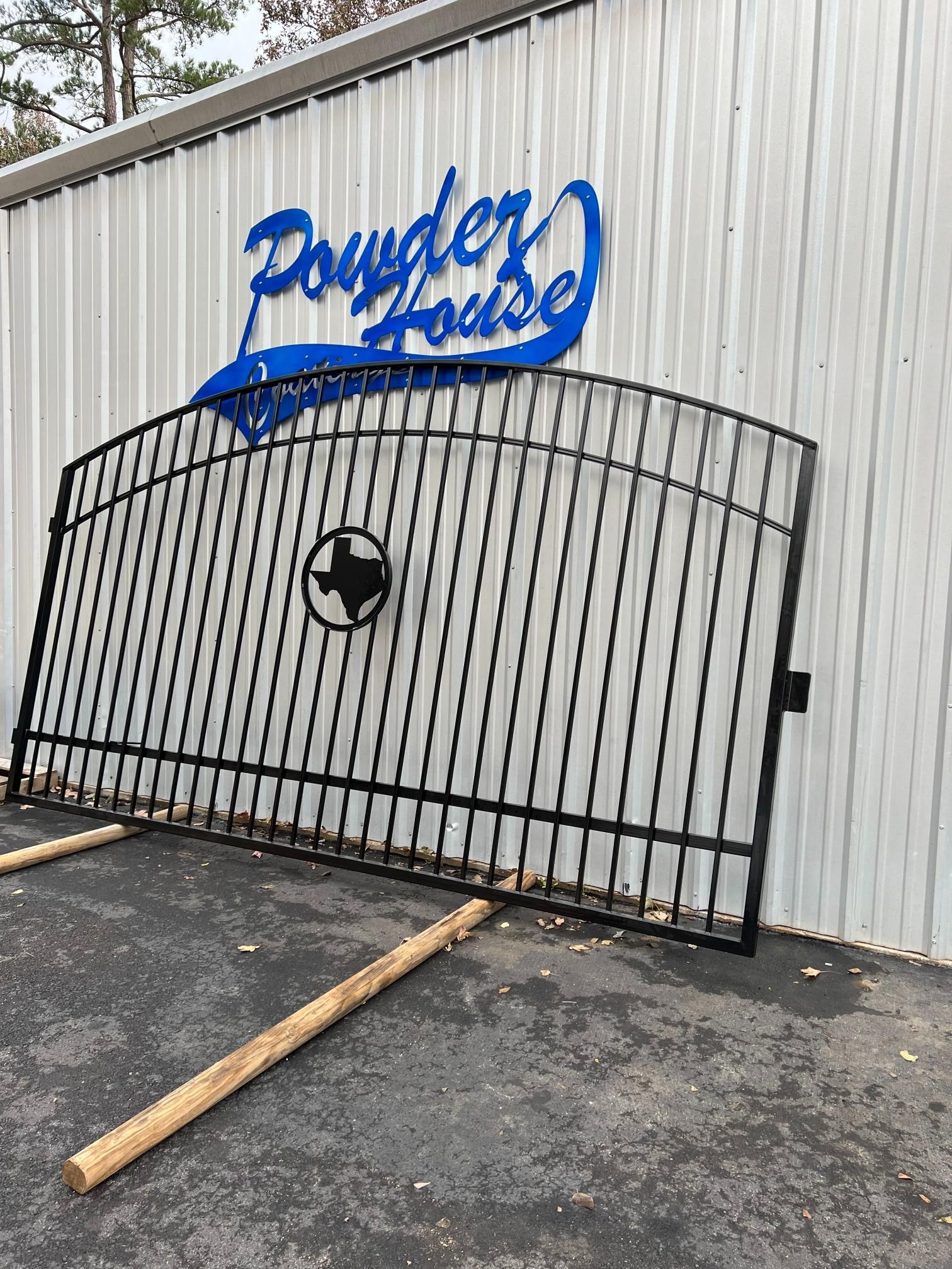 A black metal gate featuring a Texas state silhouette emblem stands against a white building with a blue Powder House sign.