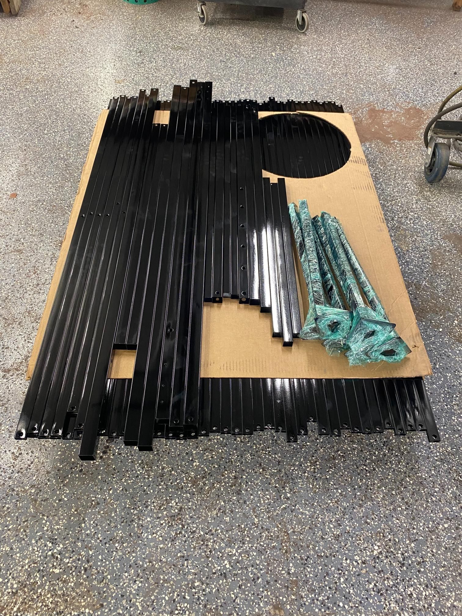 Black metal components and several turquoise-patinaed ornate metal brackets are laid out on cardboard on a concrete floor.