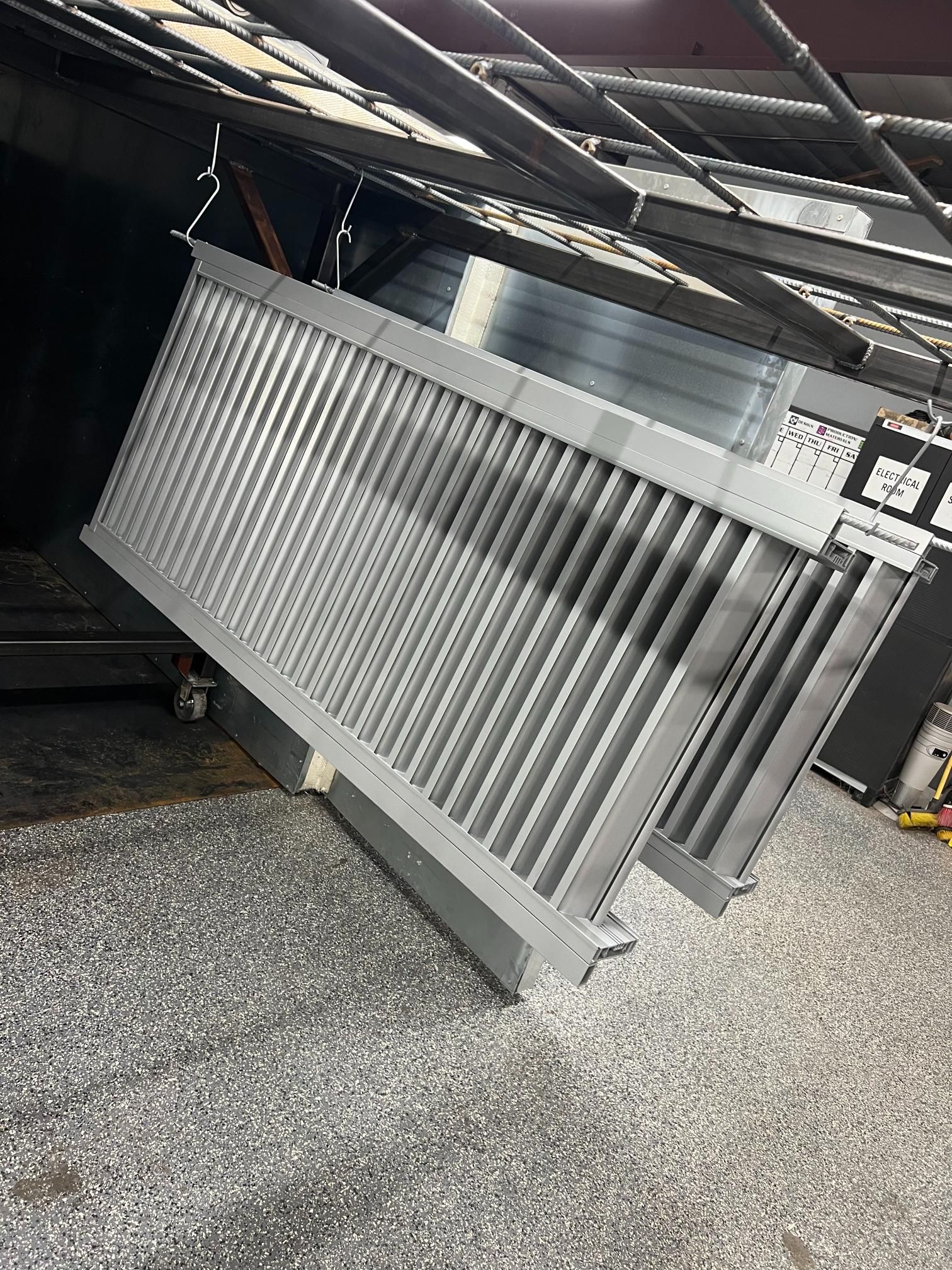 A silver, rectangular, finned metal heat exchanger hangs from an overhead industrial track in a workshop.