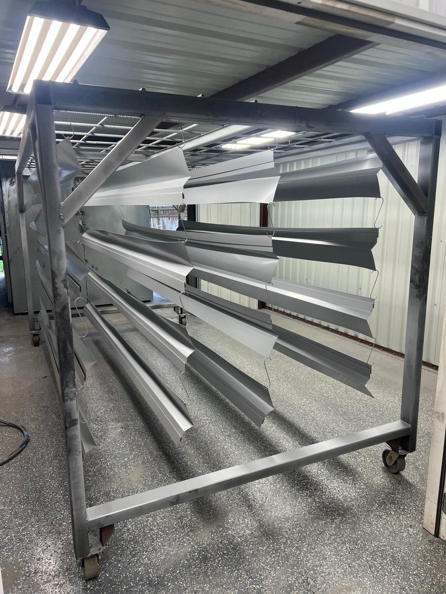 A rolling metal rack in a workshop holding several long, freshly painted gray and white metal panels.