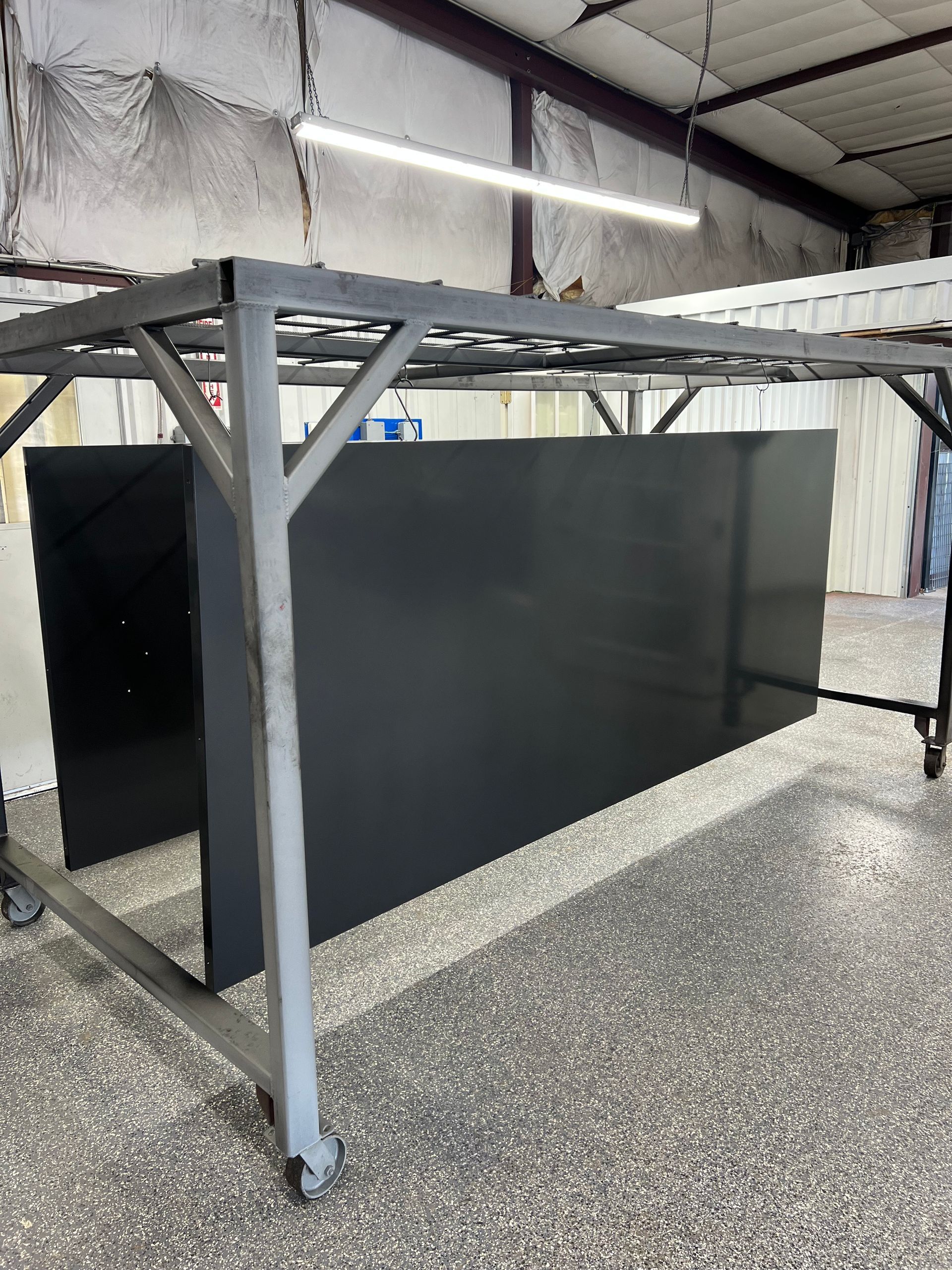 Large, metal rectangular enclosure in a workshop. Gray, with two doors. A red fan is mounted above.