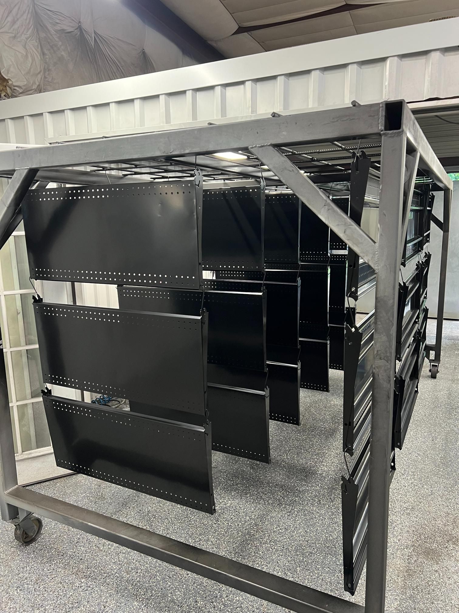 A metal rolling rack holding multiple black painted shelves in an industrial setting.