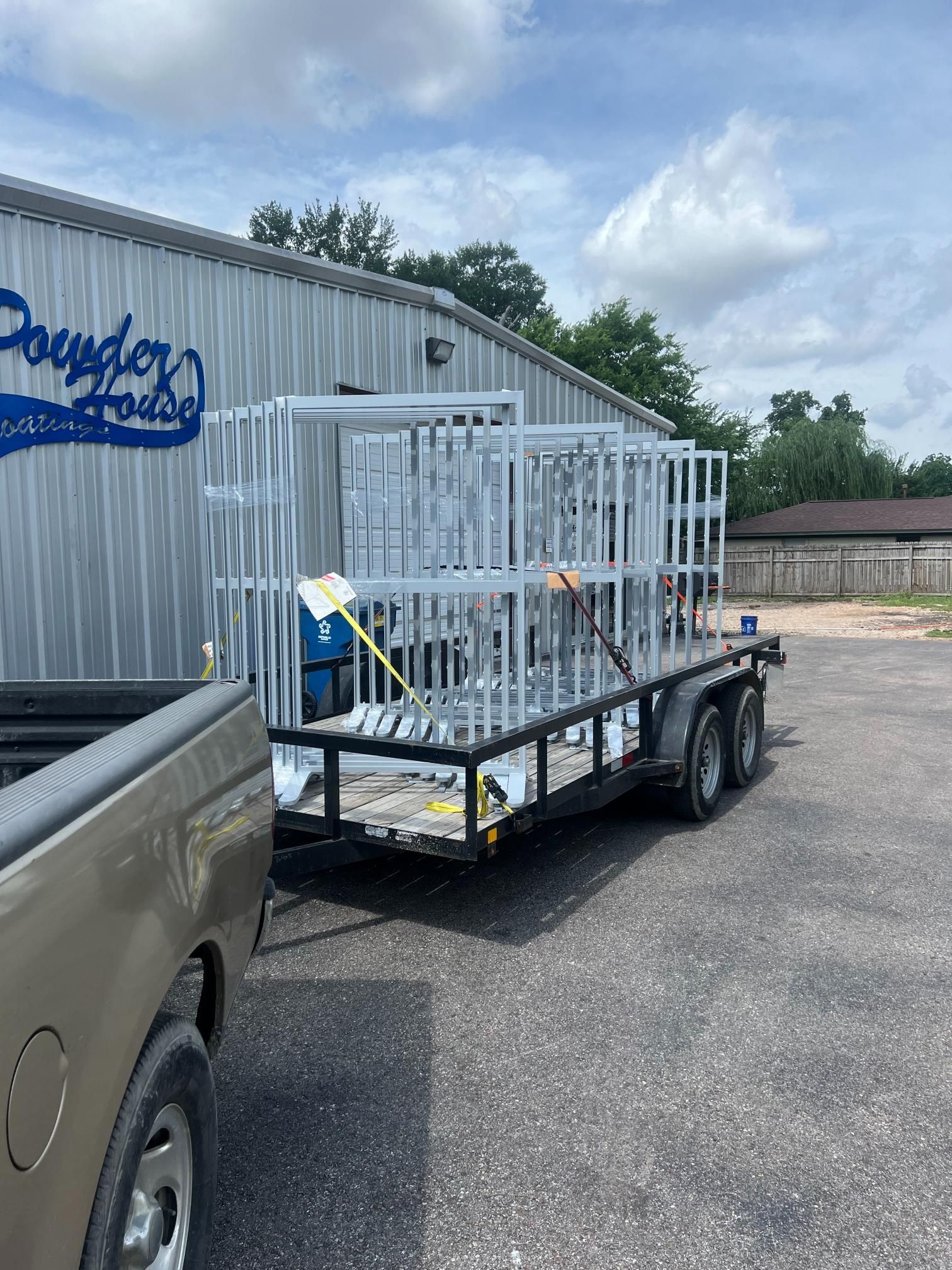 A truck pulls a utility trailer loaded with several white, metal-framed structures parked outside a business building.