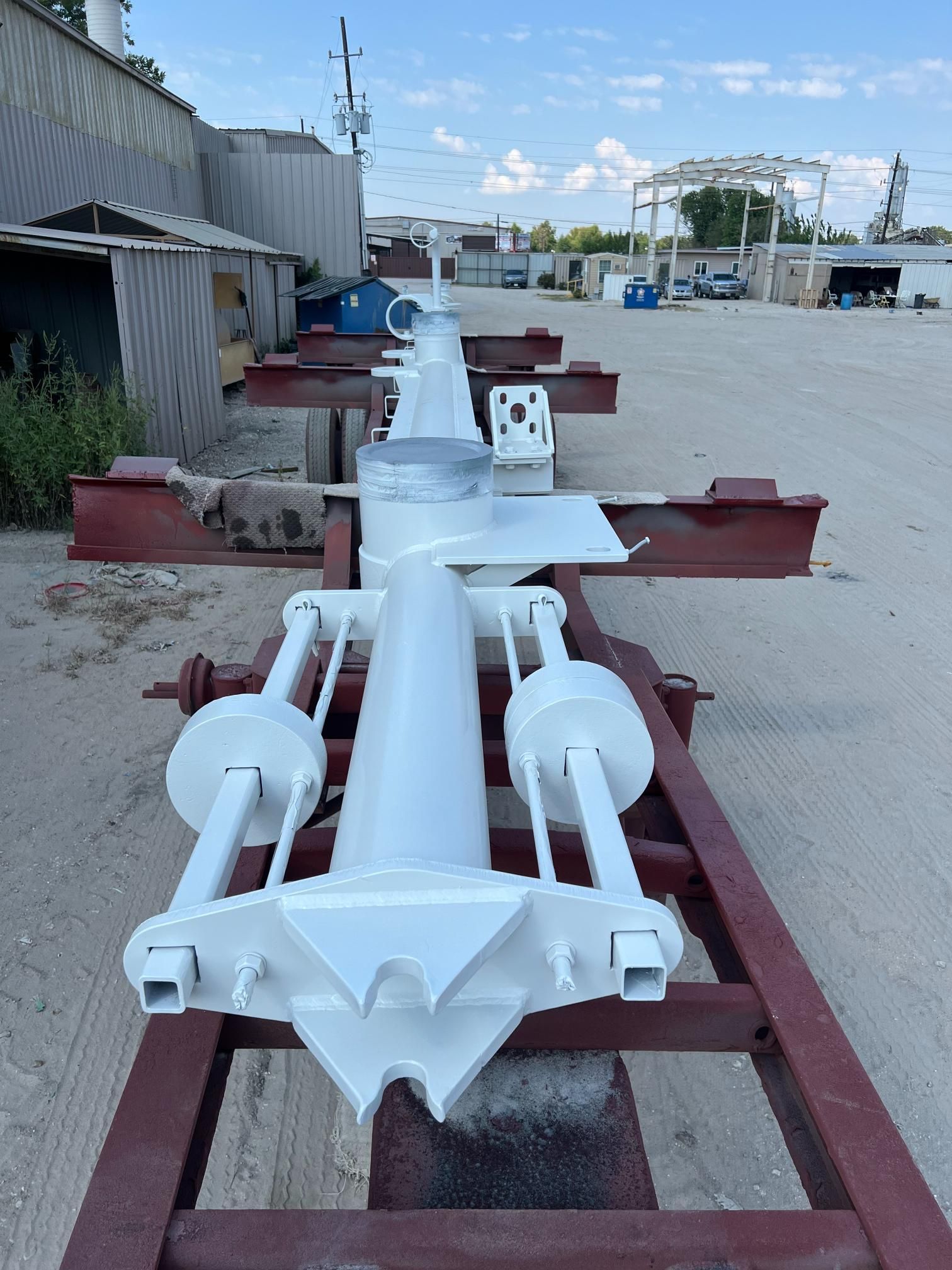 A white, freshly painted metal industrial component rests on a red steel frame in an outdoor yard.