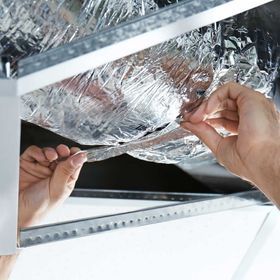 Hands securing a piece of reflective, foil-like insulation material inside a metal ceiling frame.