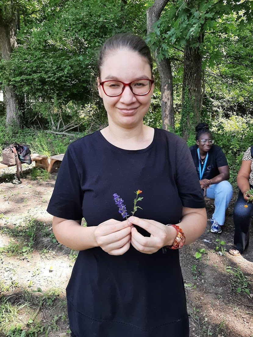 A woman wearing glasses is holding a flower in her hands in the woods.