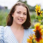 A woman in a blue dress is smiling while holding a sunflower.