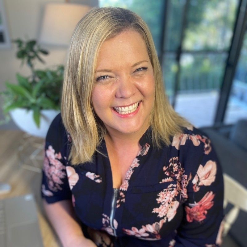 A woman in a floral shirt is smiling while sitting on a couch.