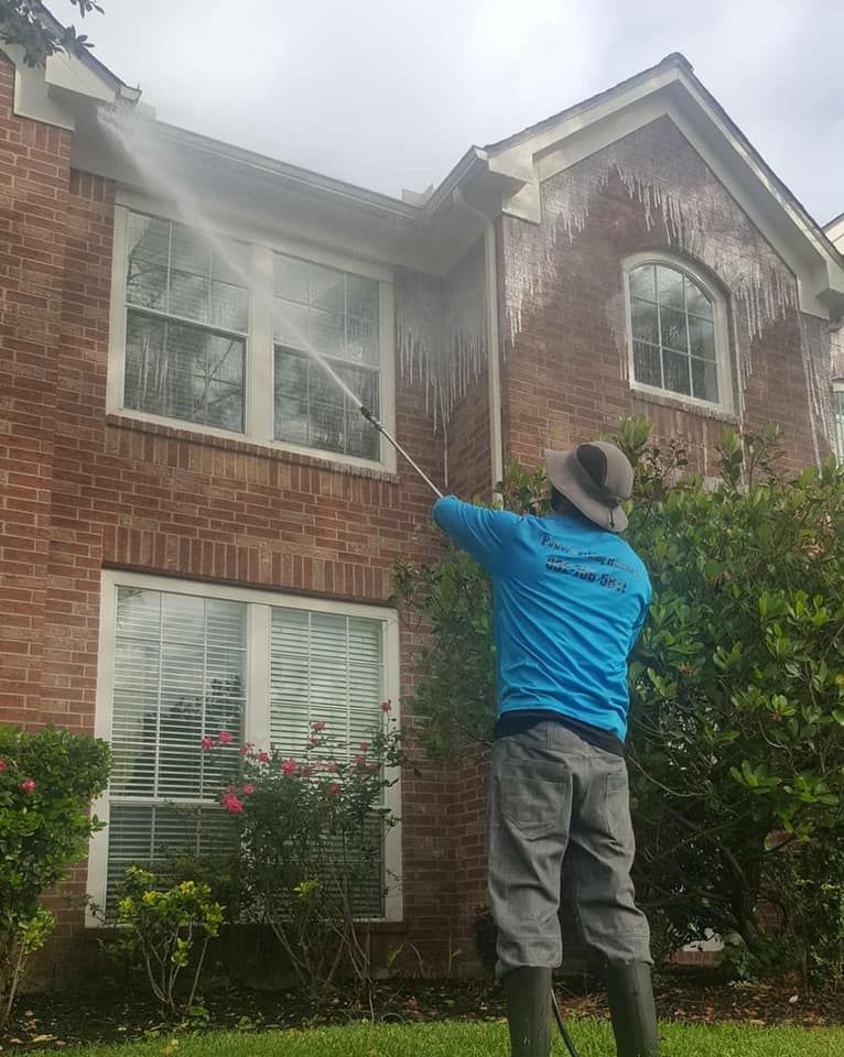 A man is cleaning a brick house with a high pressure washer.