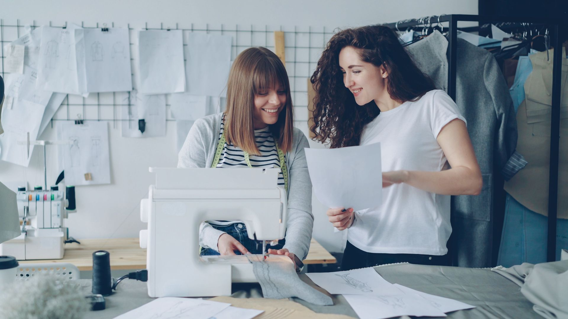 Two designers review fabric samples and sketches at a worktable in a bright studio.