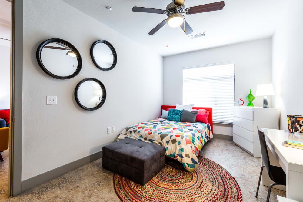 Apartment bedroom with a bed, ottoman, desk, and ceiling fan at Regents West at 24th in Austin, TX, near West Campus.