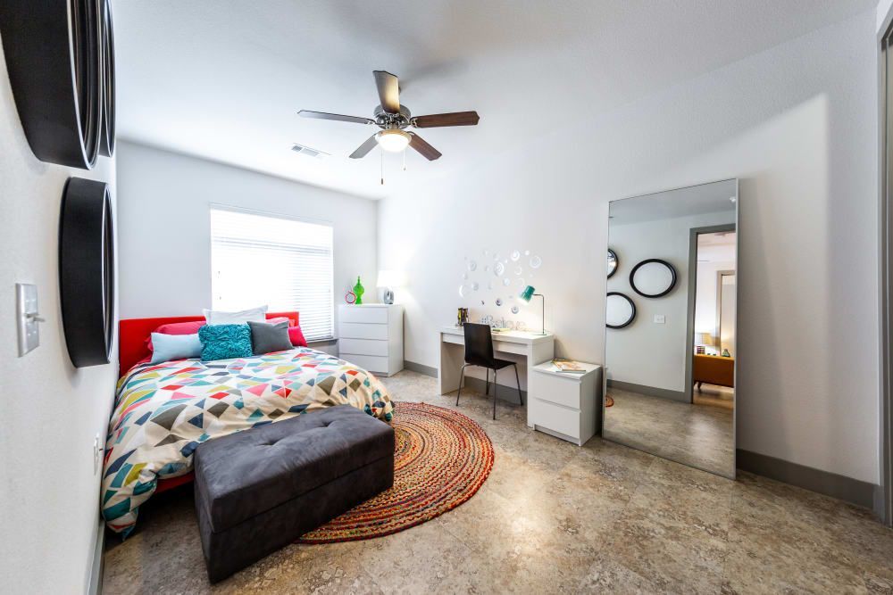 Student apartment bedroom with a large bed, a desk, a mirror, and a ceiling fan at Regents West at 24th in Austin, TX, near West Campus.