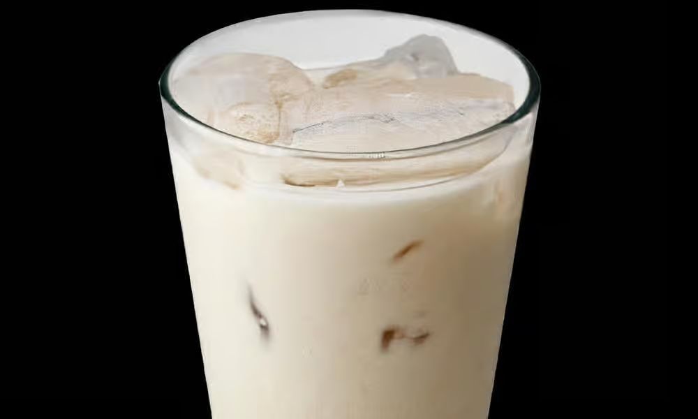 Tall glass of iced beverage, creamy white with ice cubes, against a black background.