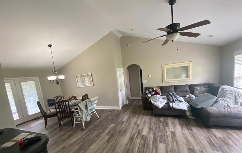 Open living-dining room with gray sectional, dining table, ceiling fans, and wood flooring