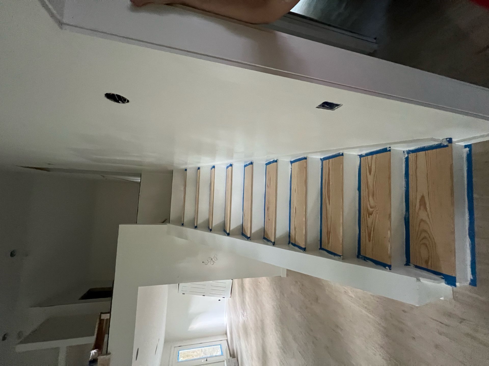 Staircase under construction with taped white walls and exposed wood steps in a narrow interior space