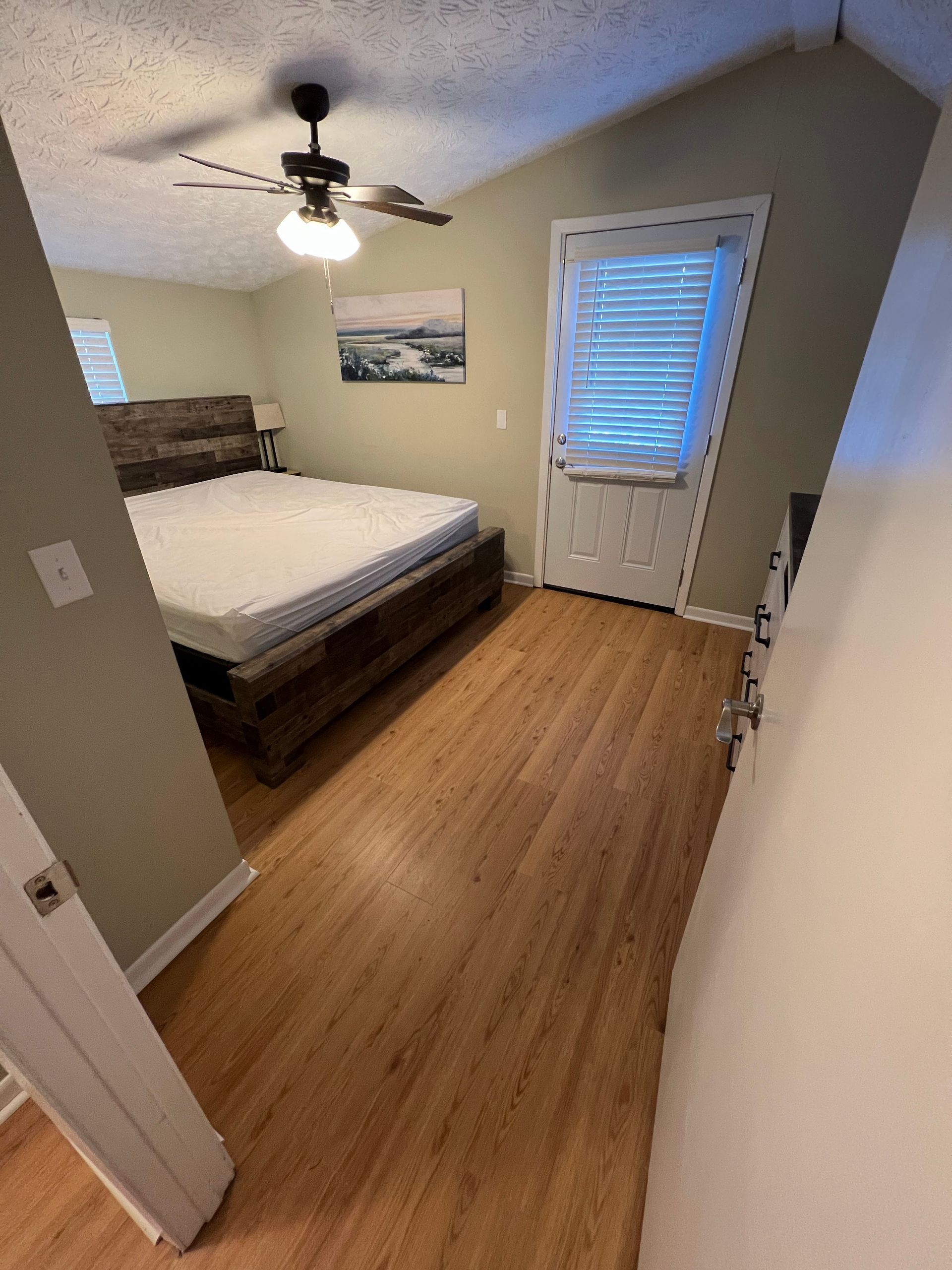 Small bedroom with a bed, ceiling fan, window blinds, and wood-look flooring.
