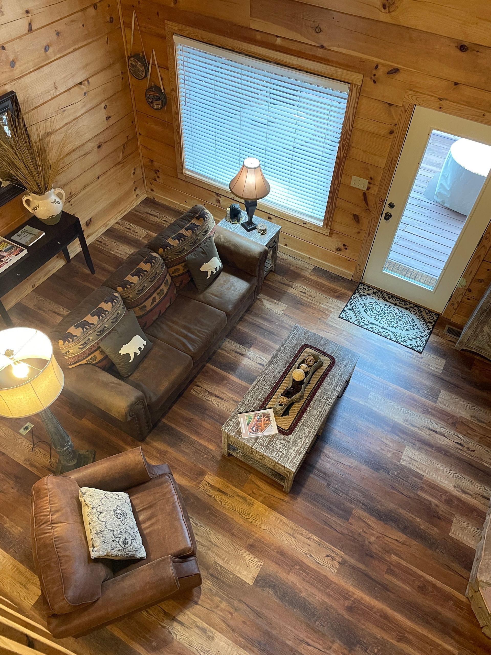 Cozy log cabin living room with leather chairs, coffee table, lamps, and large windows.