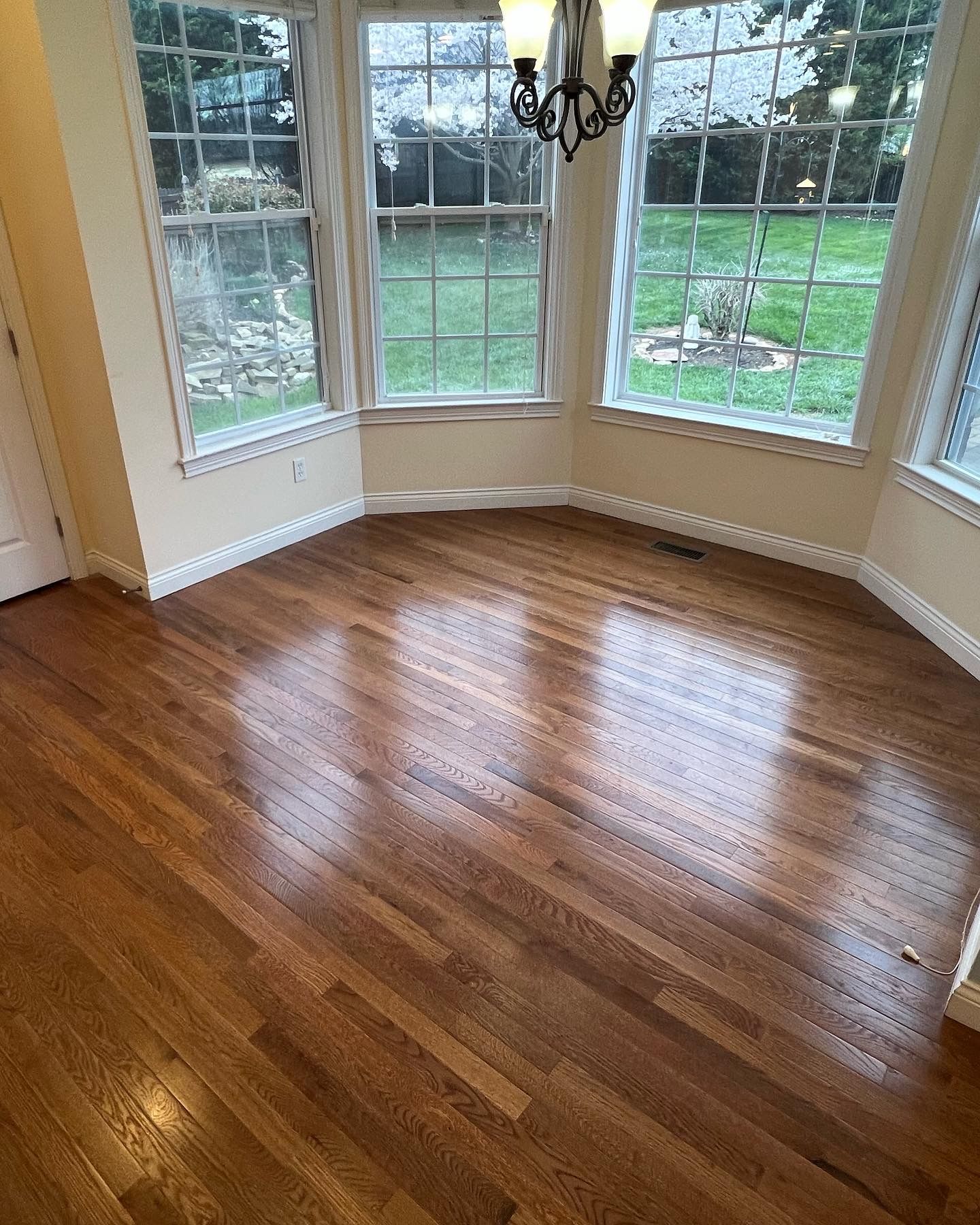 Bright empty room with hardwood floor, large bay windows, and a hanging chandelier.