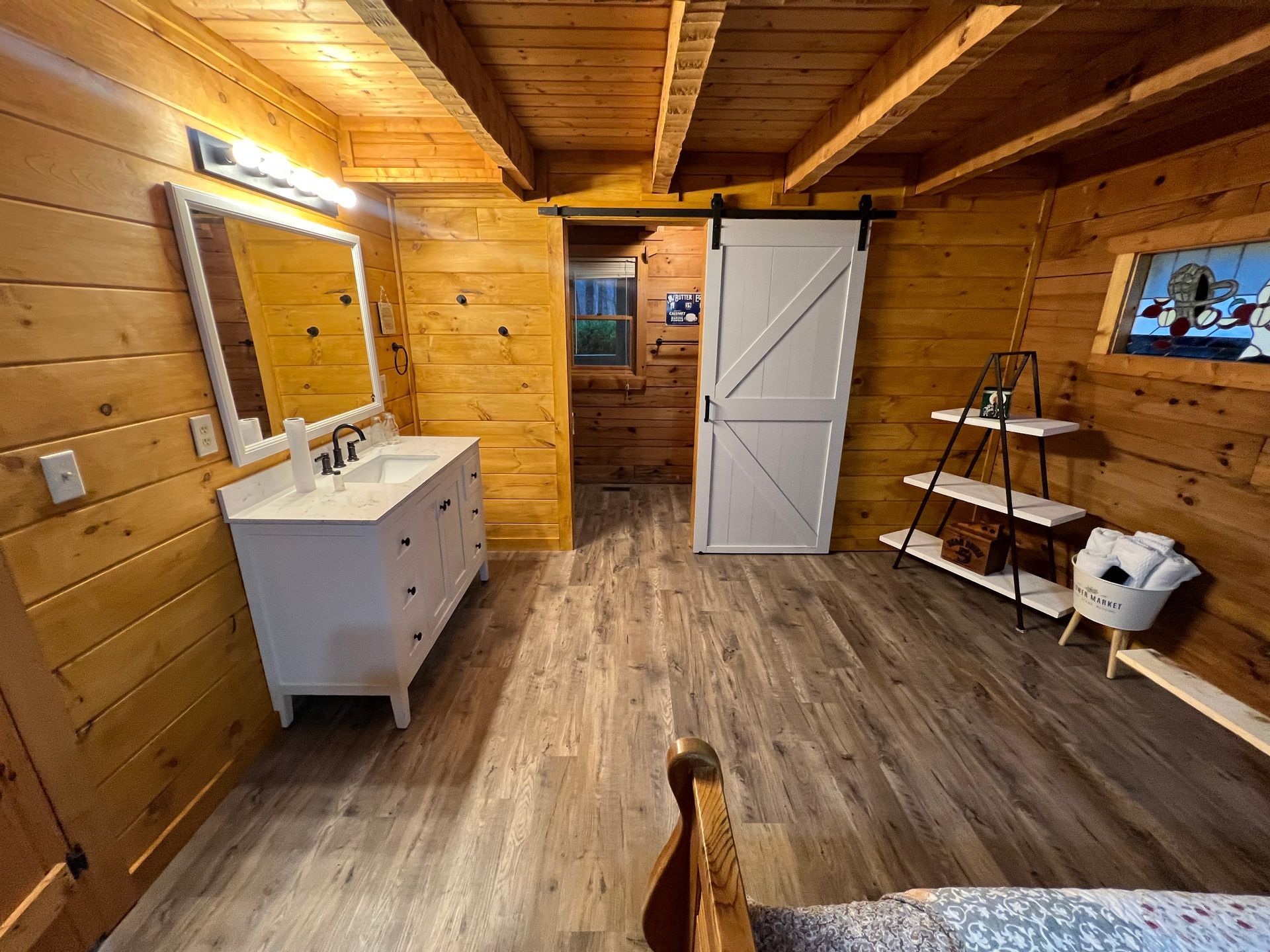 Rustic wooden bathroom with vanity, mirror, white door, and shelves on the right