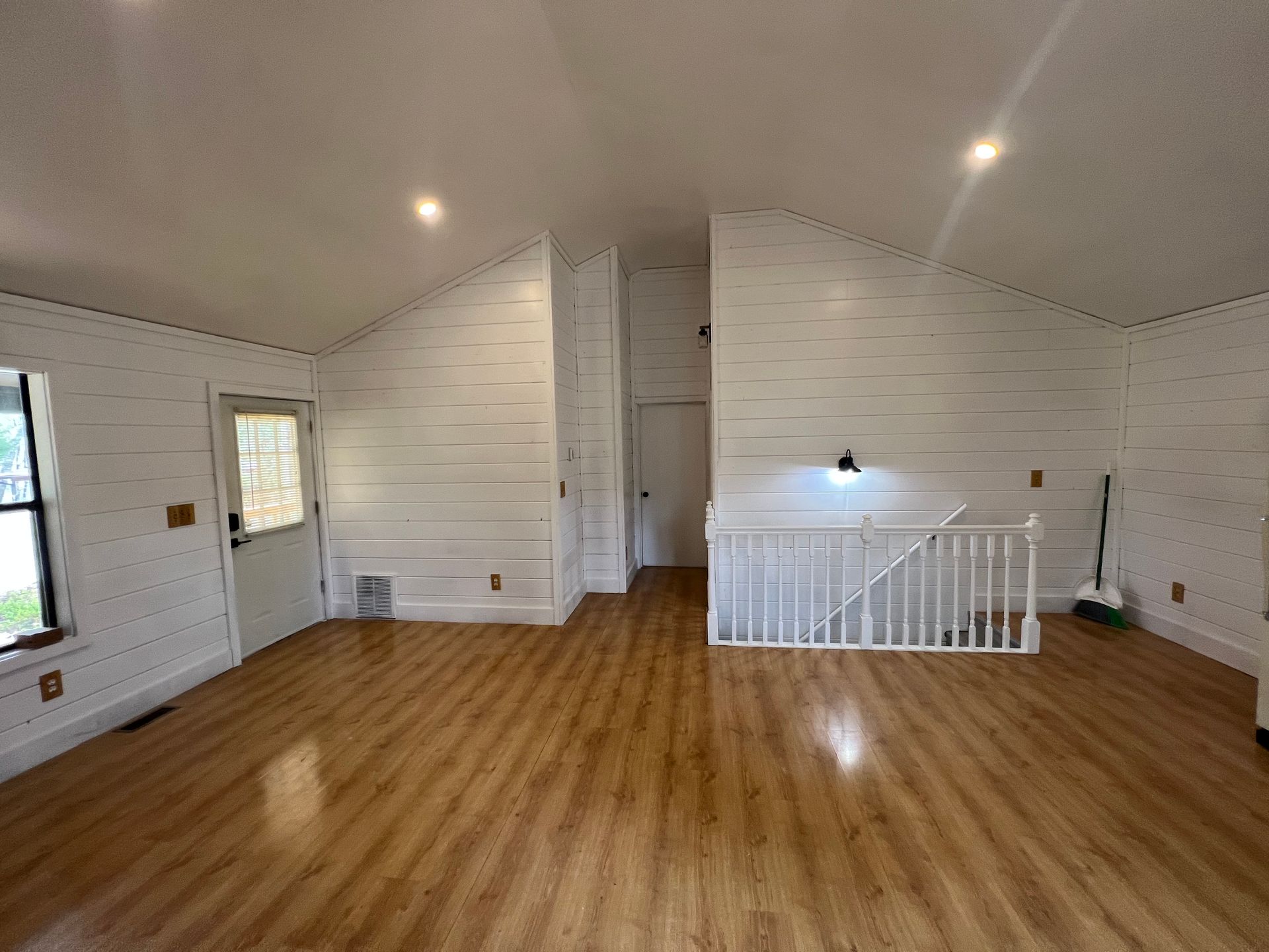 Empty white living room with wood floors, staircase railing, and recessed ceiling lights