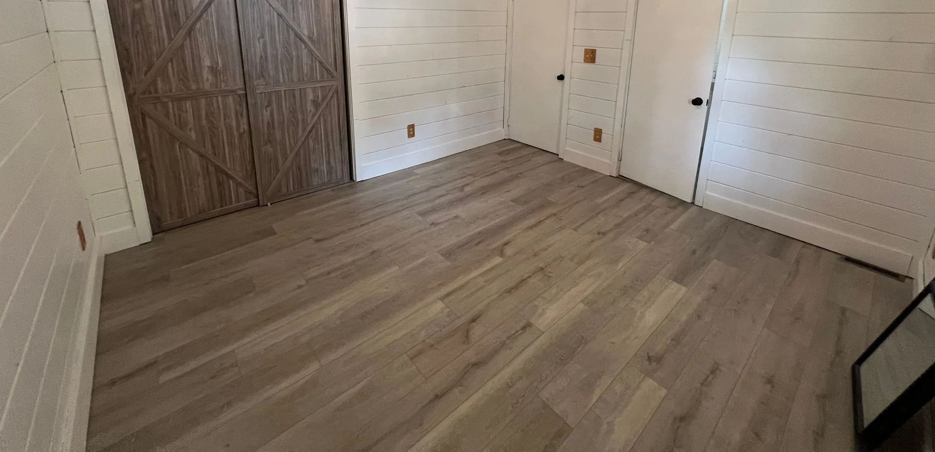 Empty white room with wood-look floors and a closed paneled door