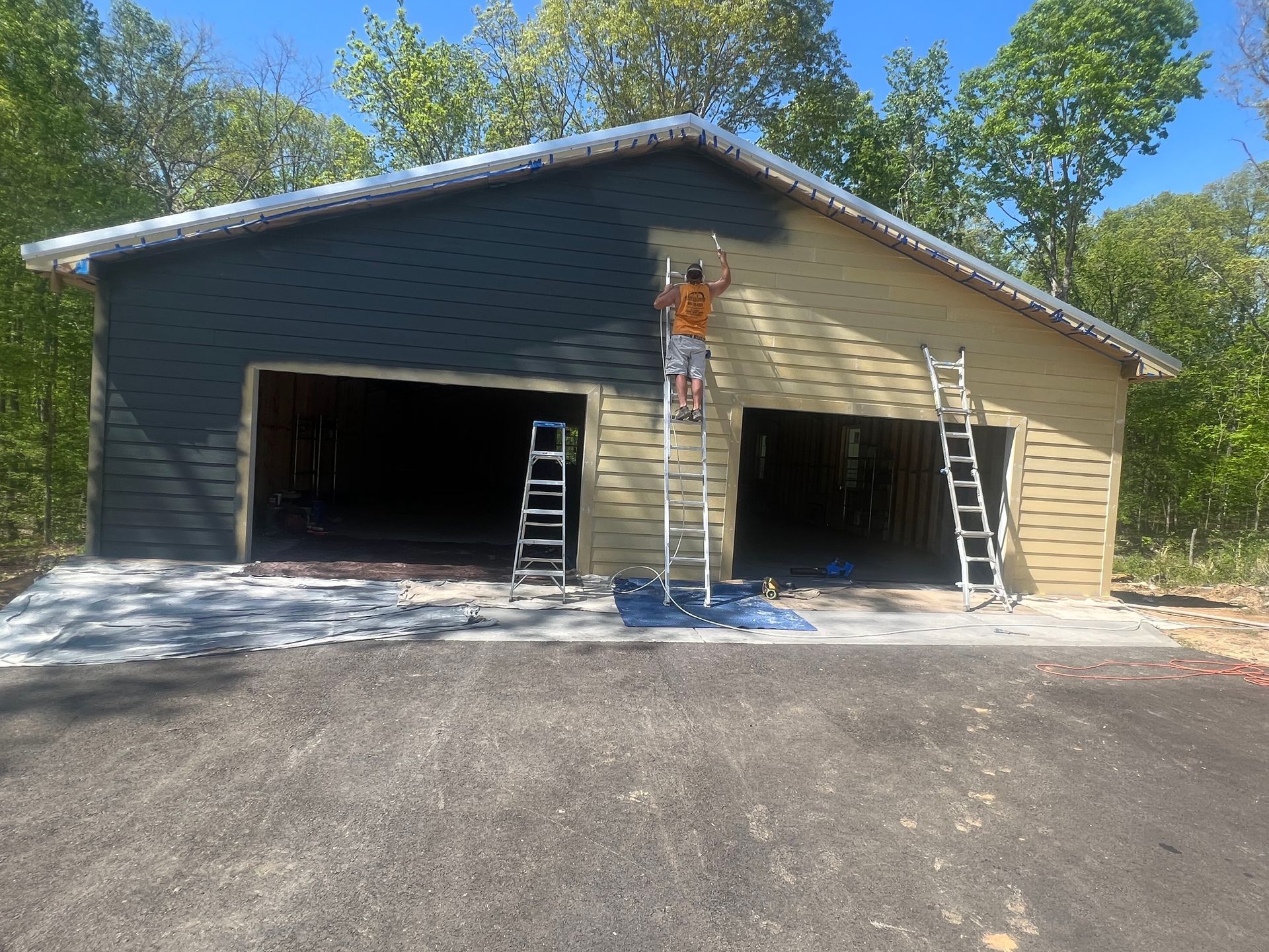 Garage under construction with two open bays, ladders, and workers on the front wall