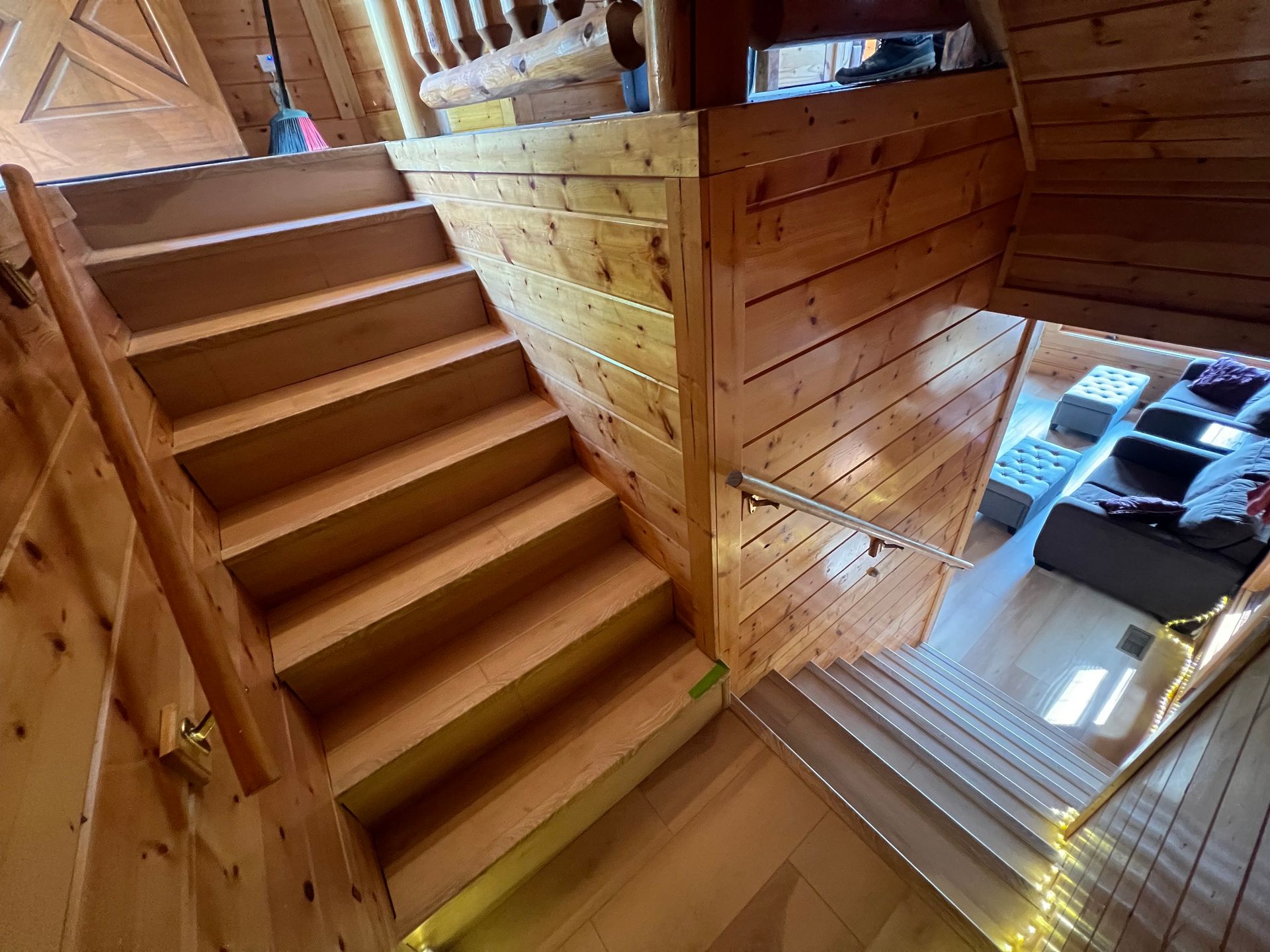 Wooden indoor staircase beside a loft, with natural light and a small living area below