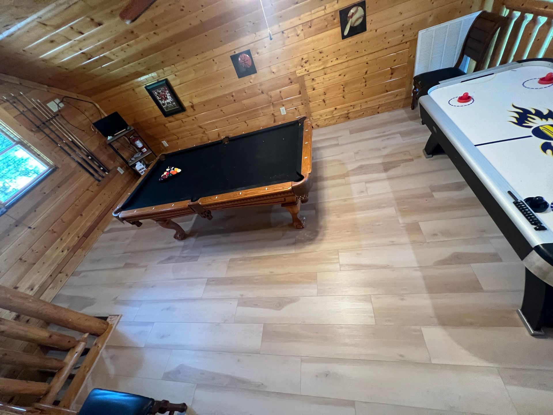 Wood-paneled game room with a pool table and air hockey table on a light wood floor.