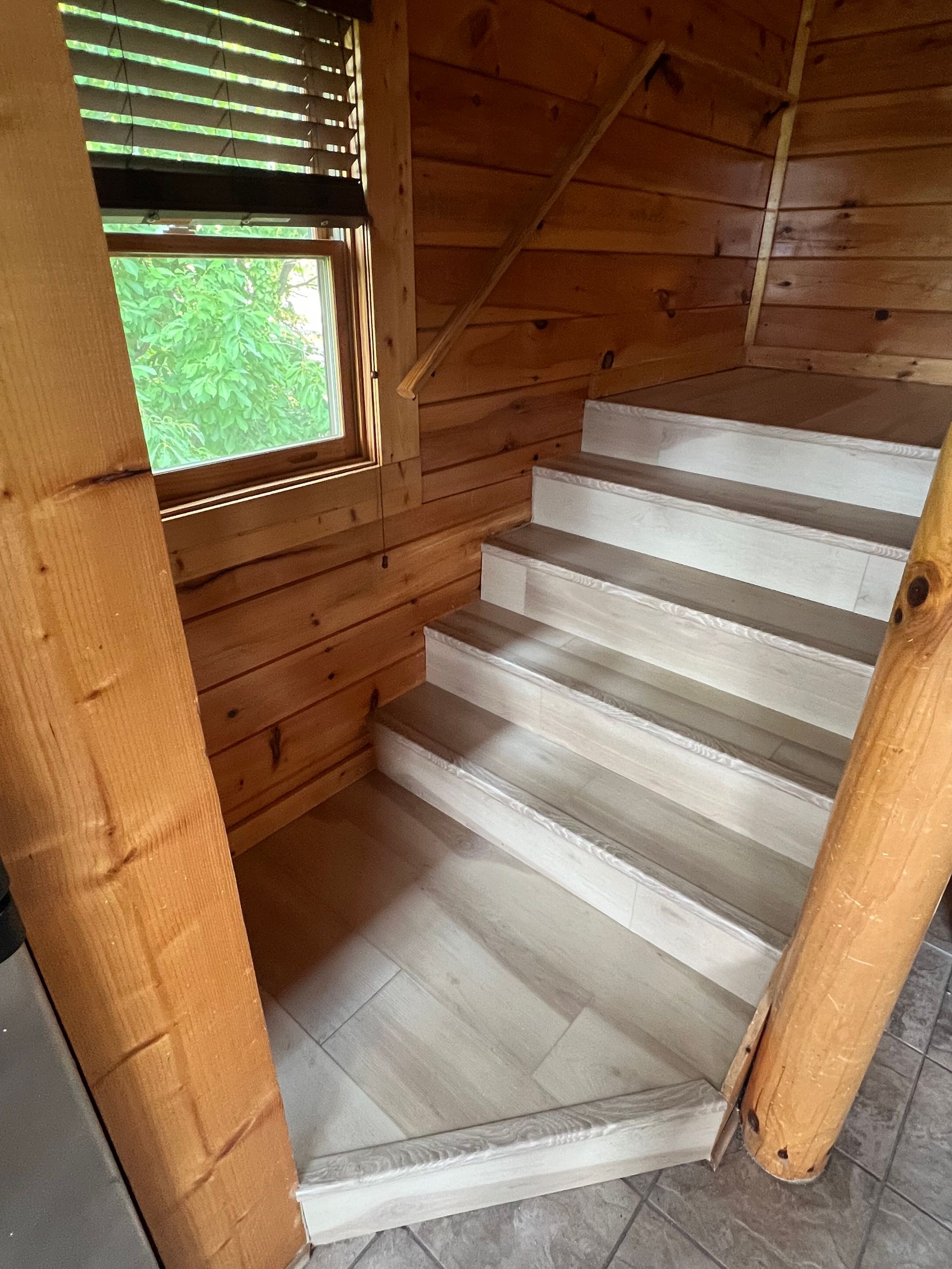 Interior wooden staircase with white steps in a log cabin, next to a window.