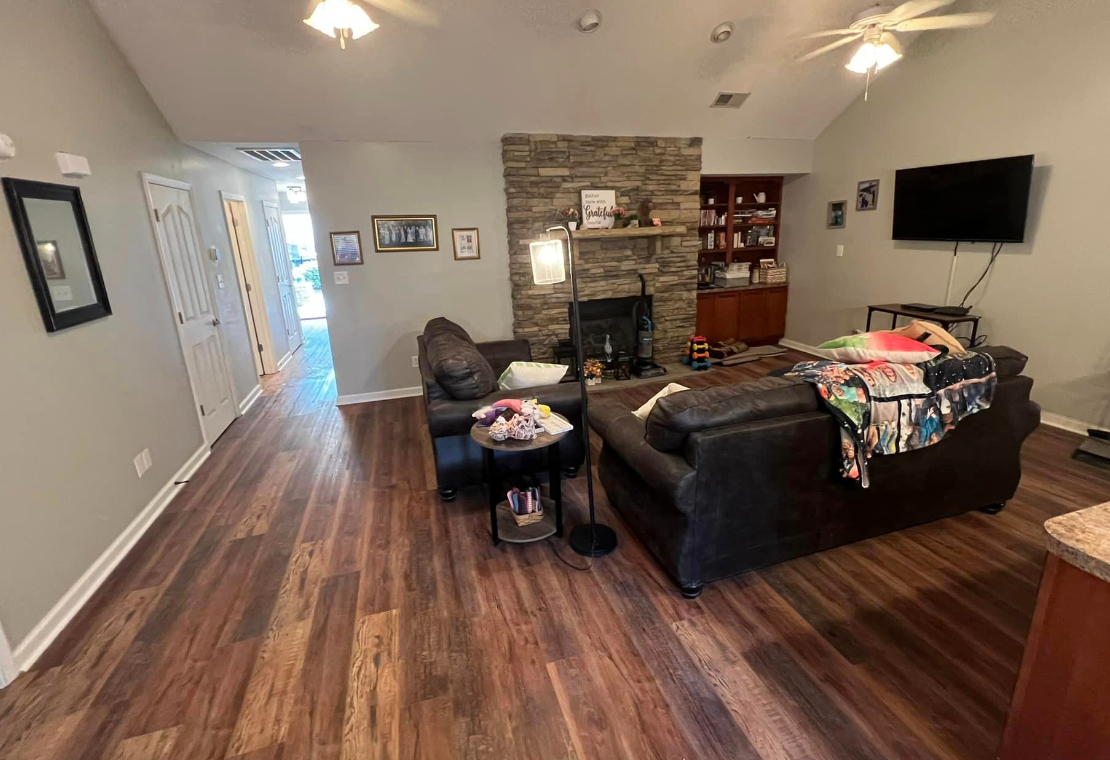 Spacious living room with wood floors, dark sofas, TV, and a lit fireplace.