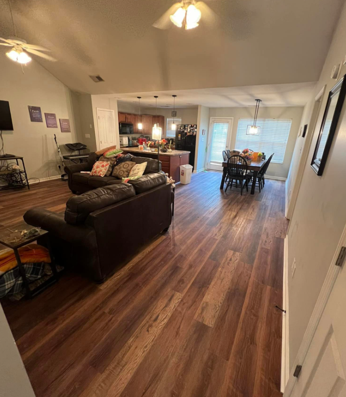 Open-concept living and dining room with dark sectional, wood floors, and sliding glass door.
