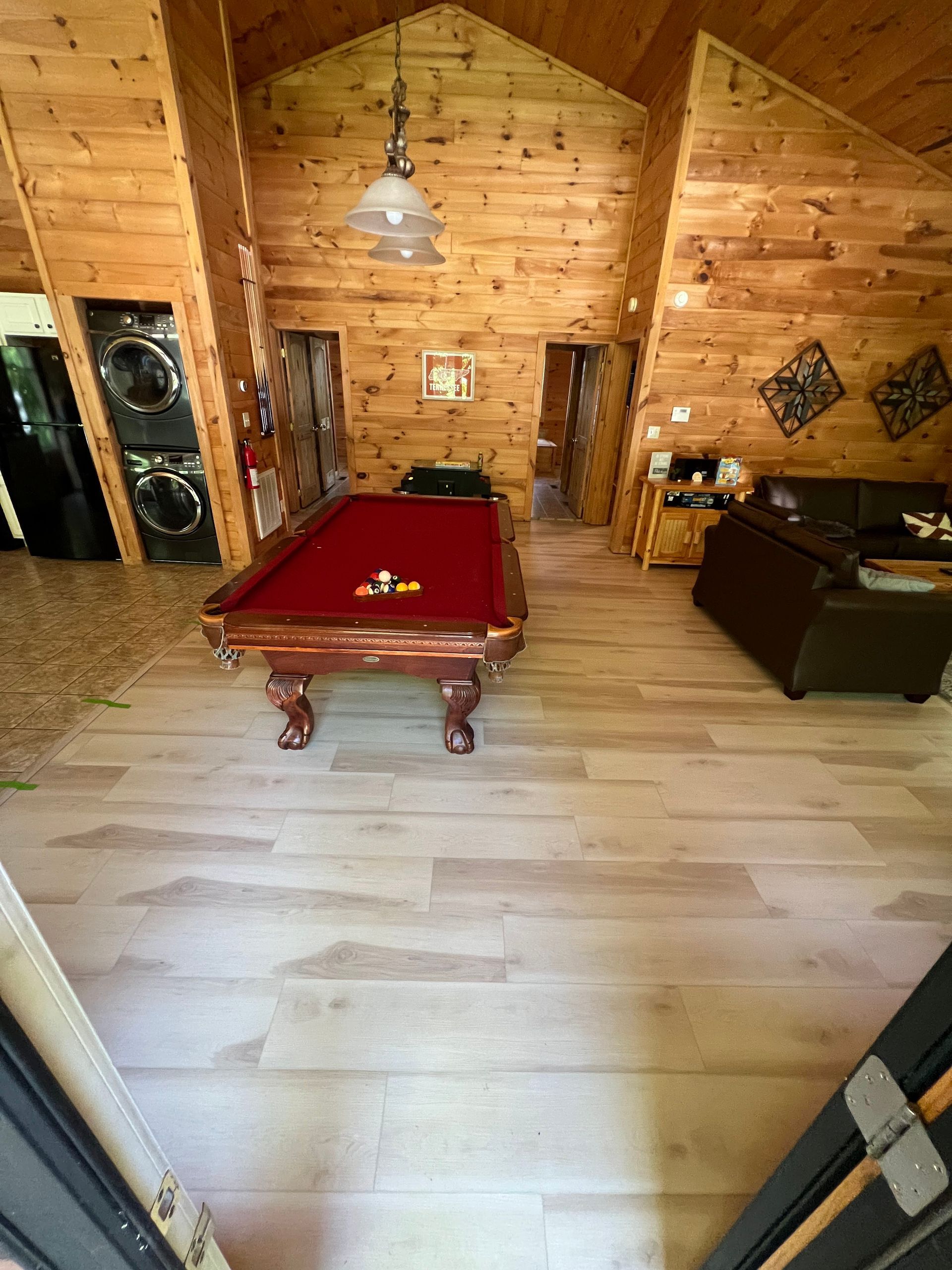 Wood-paneled game room with a red pool table, hanging light, and seating area