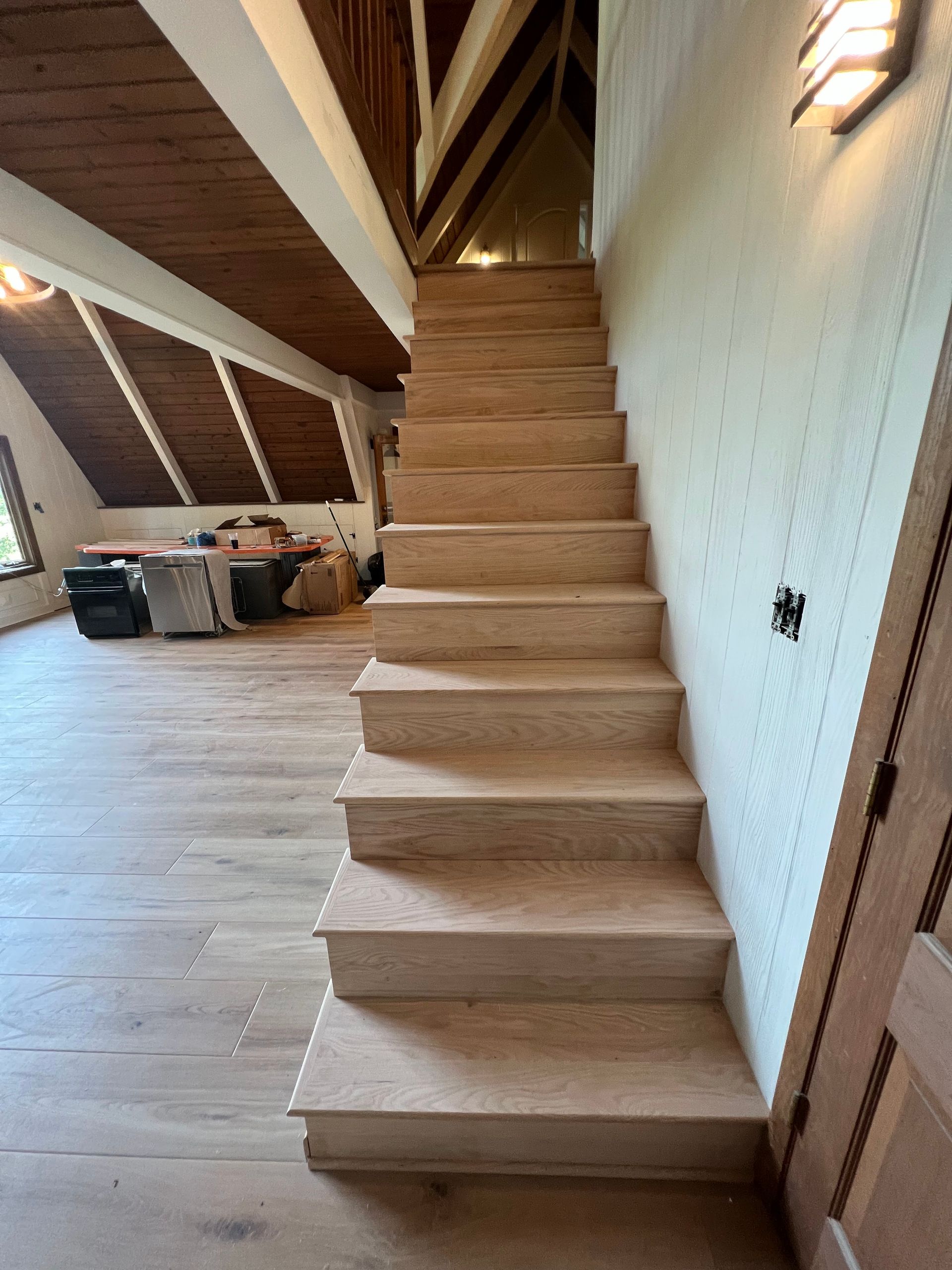 Narrow carpeted staircase in an unfinished attic hallway with sloped ceiling and exposed beams