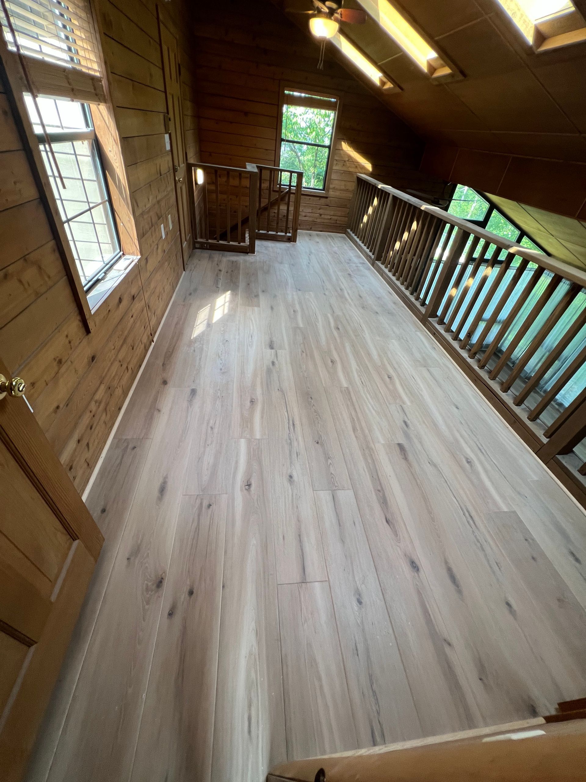 Wood-paneled porch with white floorboards, railing, and windows, lit by warm overhead lights