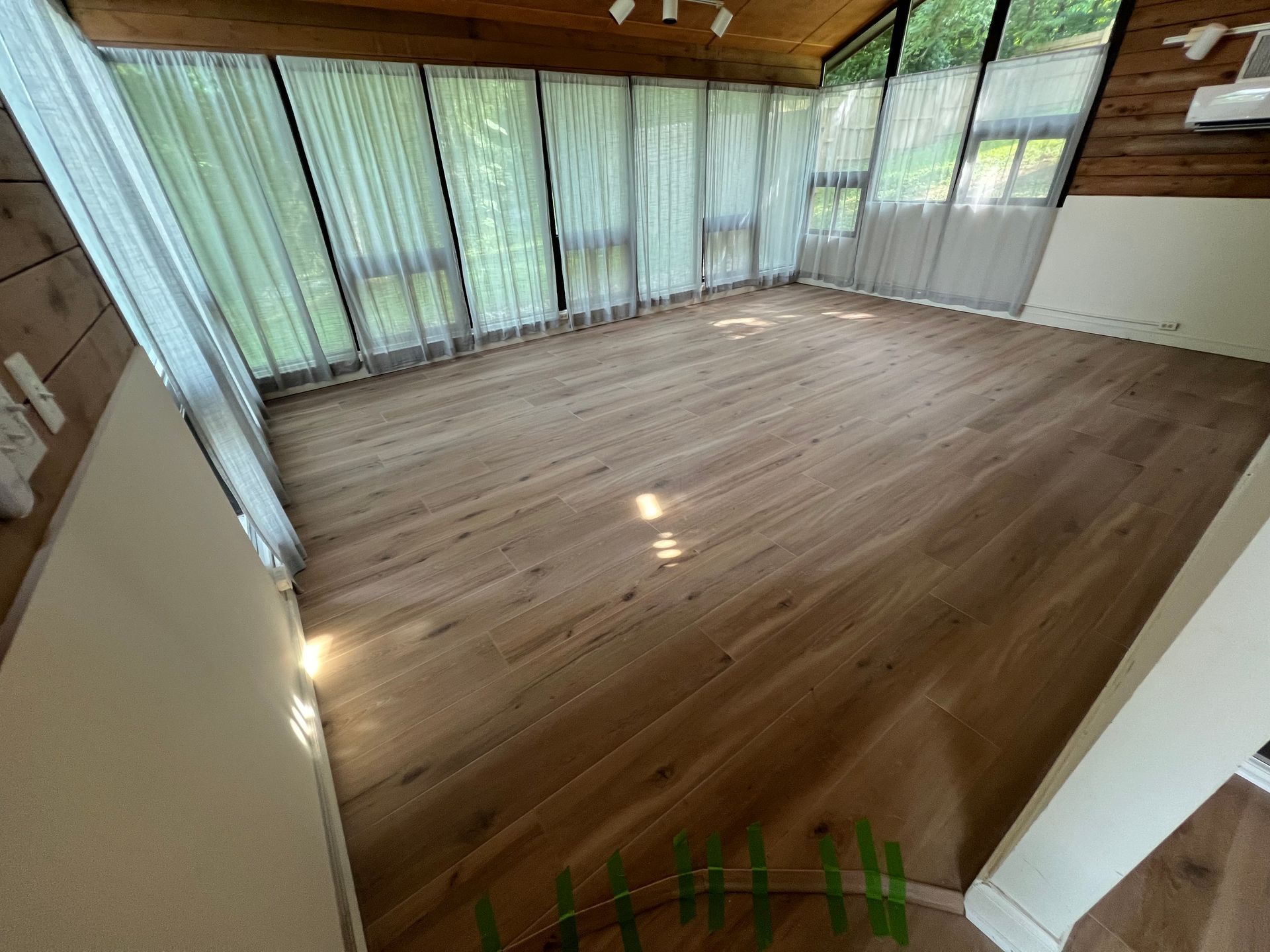 Empty sunroom with wood floors, tall windows, and sheer curtains letting in soft daylight