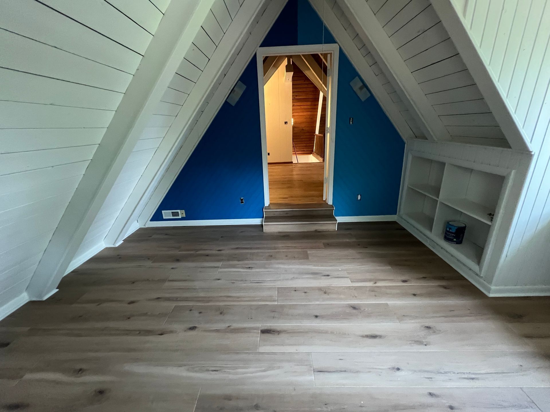 Empty attic room with sloped white walls, blue accent wall, and wood plank floor.