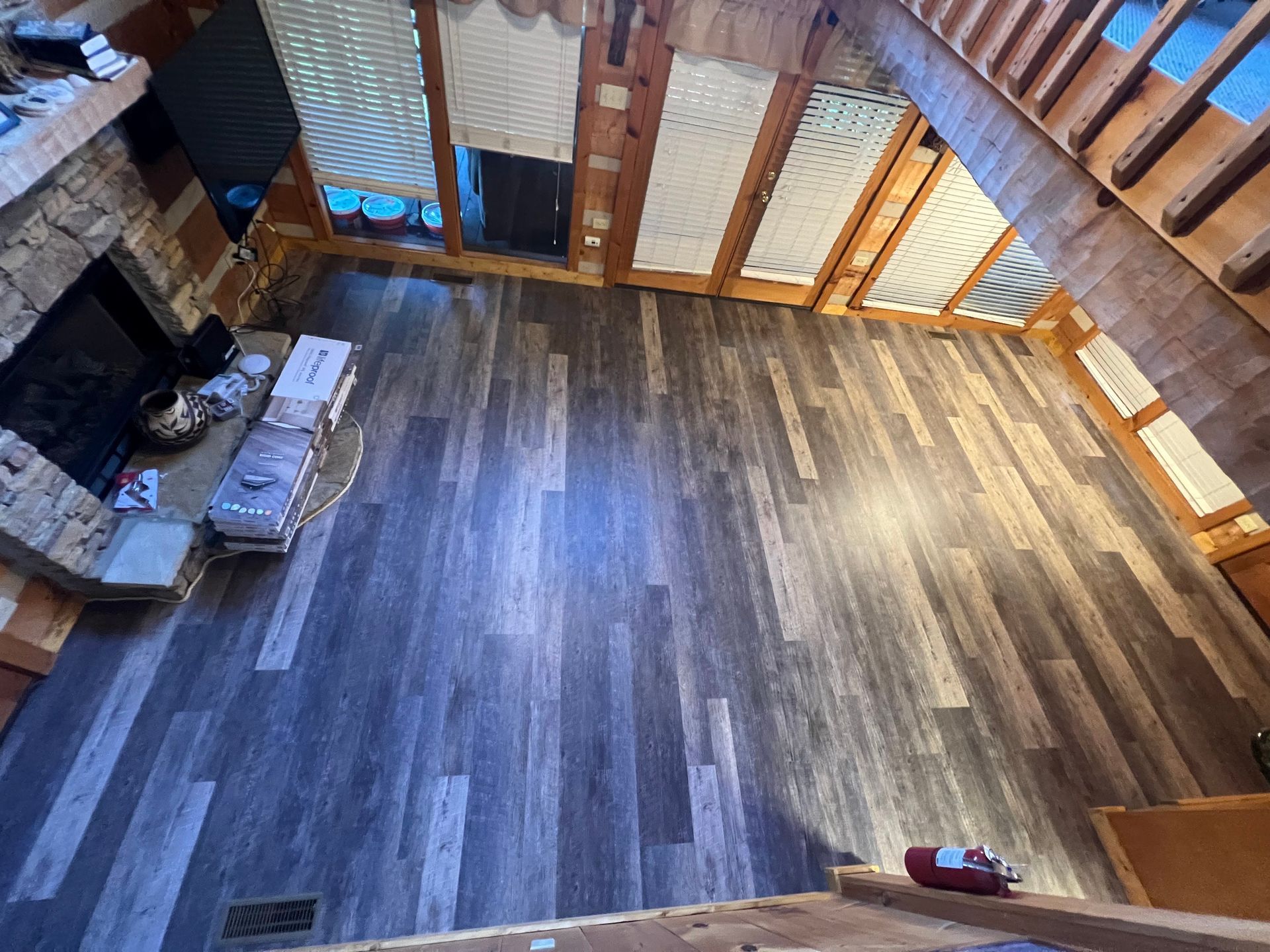 Spacious wooden loft with a stone fireplace, large windows, and a staircase along the right wall.