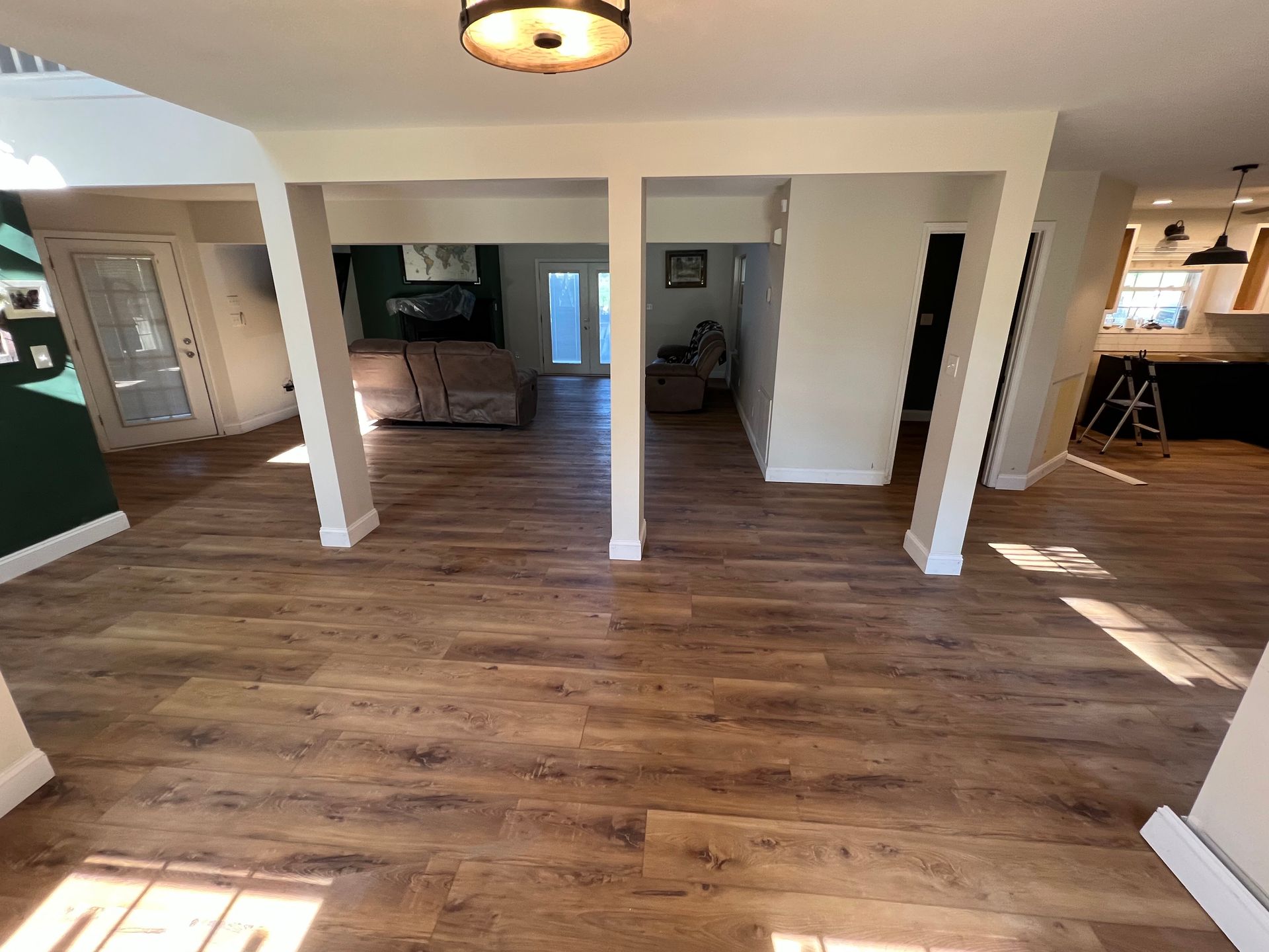 Empty open-plan room with wood floors, white columns, and sunlight streaming in from the right.