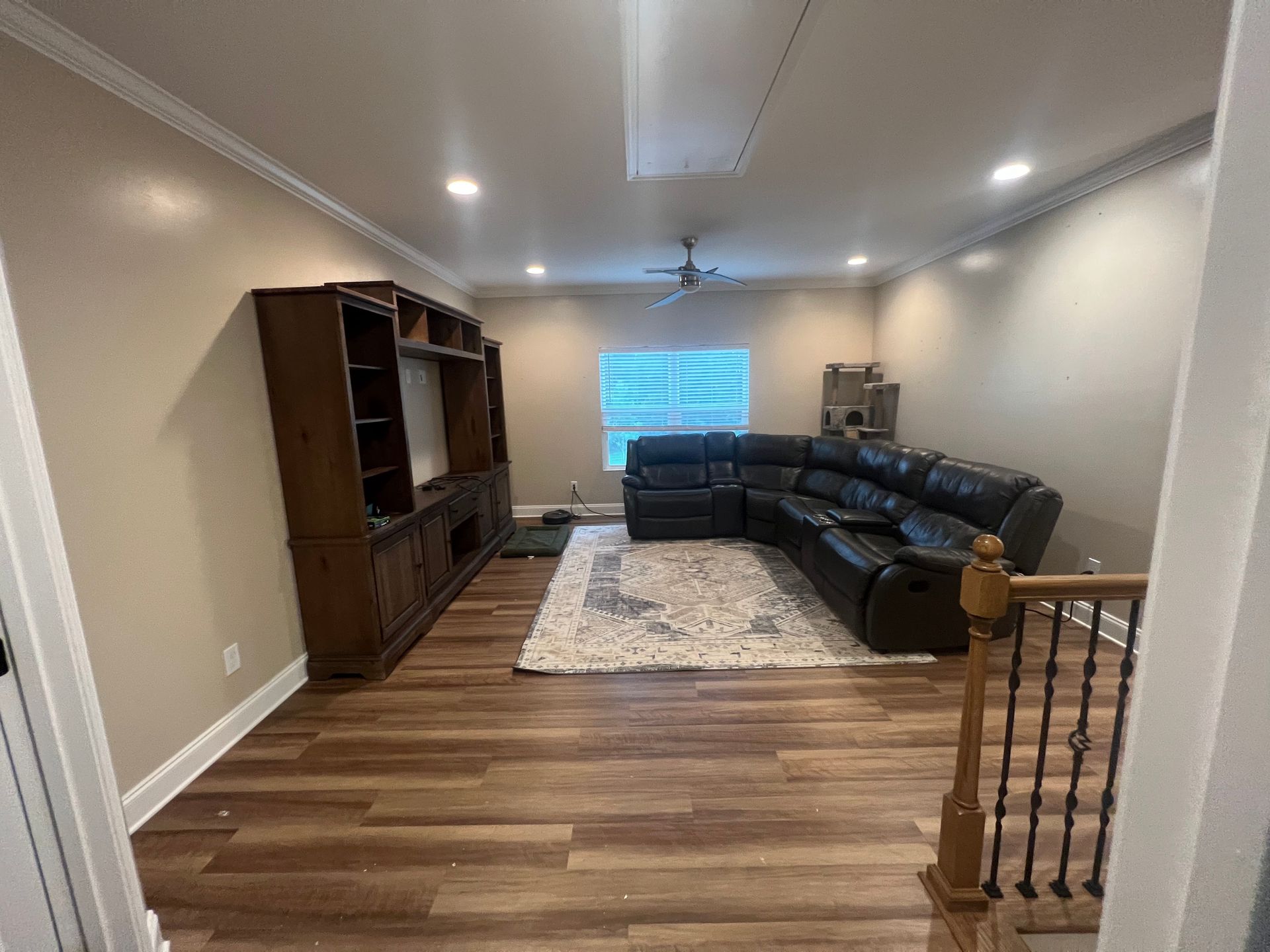 Spacious living room with wood floors, dark sectional sofa, area rug, and large cabinet along the wall.