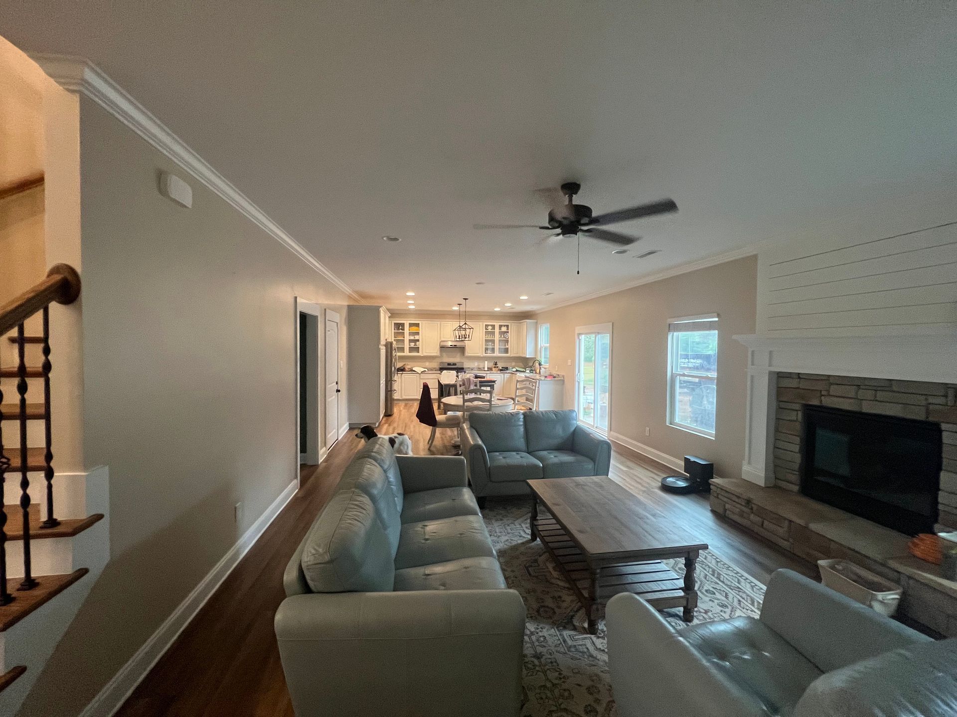 Bright living room with gray sofas, fireplace, ceiling fan, and open kitchen in the background