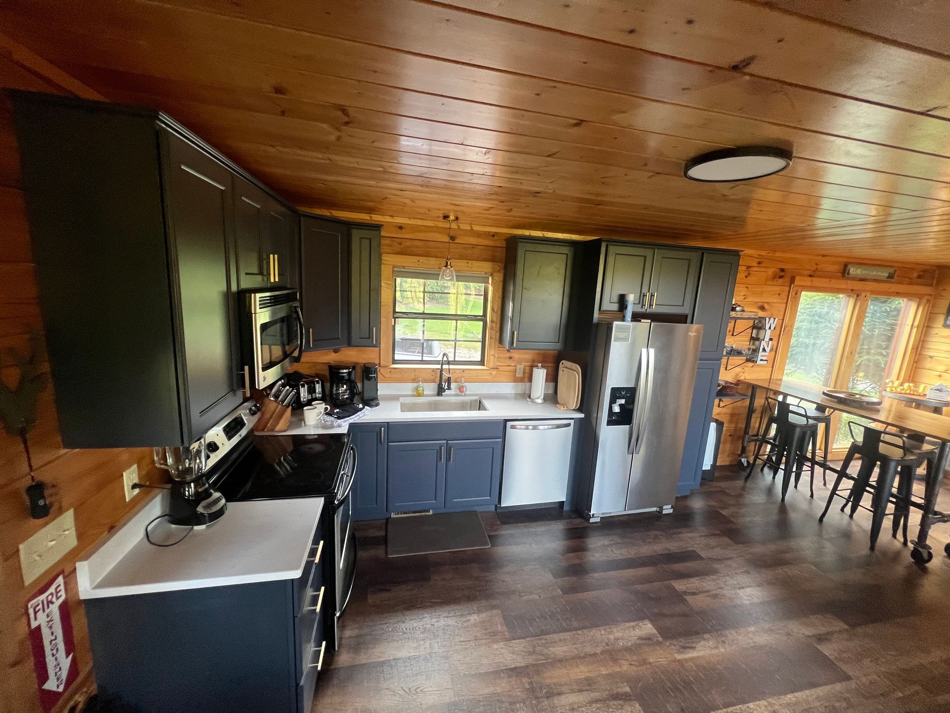 Wood-paneled kitchen with gray cabinets, stainless fridge, and dining table by windows