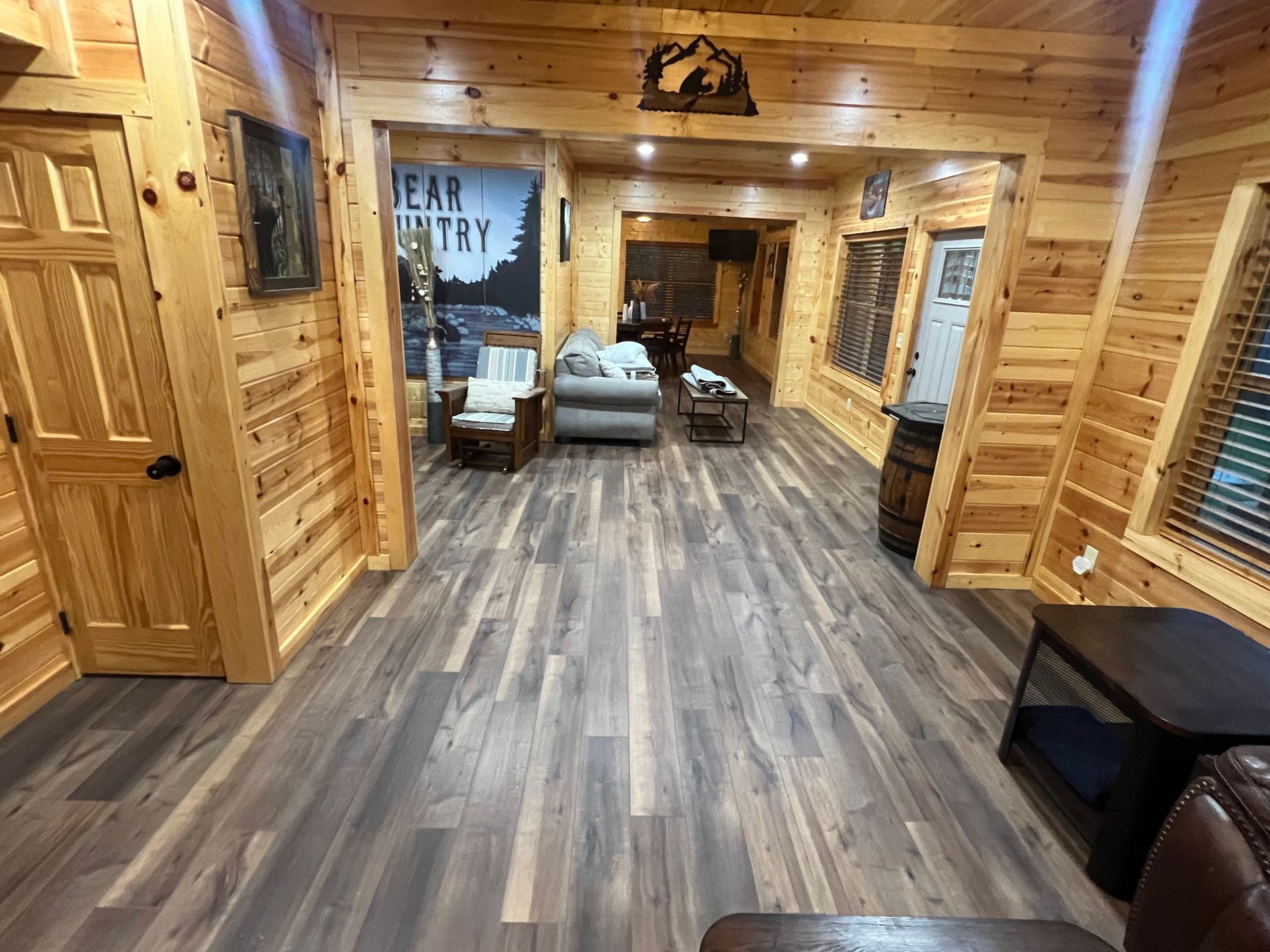 Wood-paneled cabin hallway with rustic decor, gray wood floor, and seating area at the far end.
