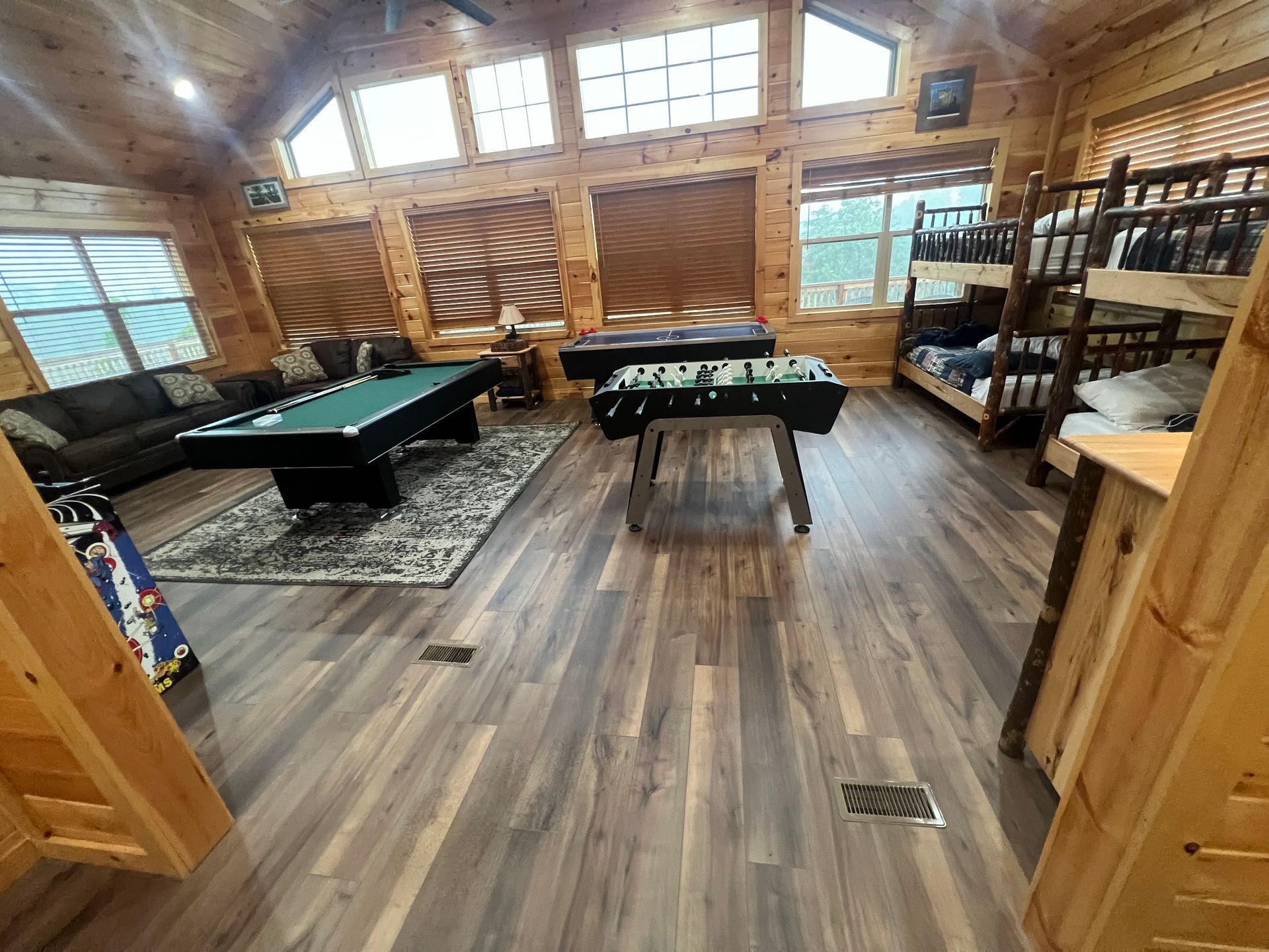 Game room with two pool tables, wood-paneled walls, large windows, and bunk beds along the right side.
