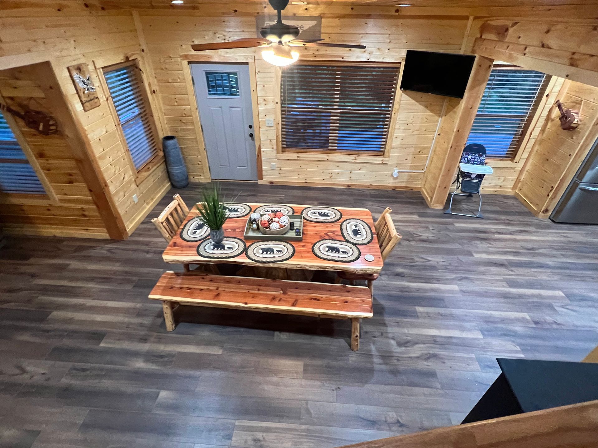Rustic dining room with a long wooden table set for a meal and large windows with blinds.