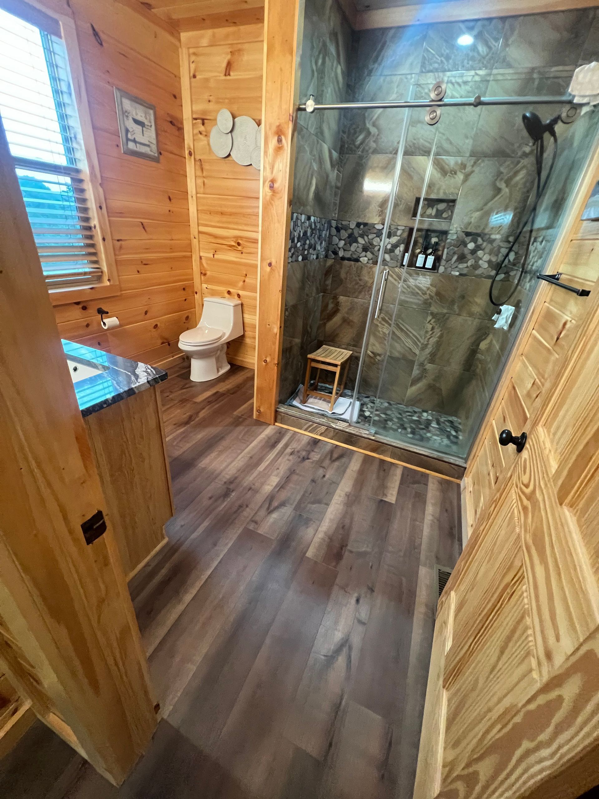 Wood-paneled bathroom with toilet, glass shower, and wood-look flooring